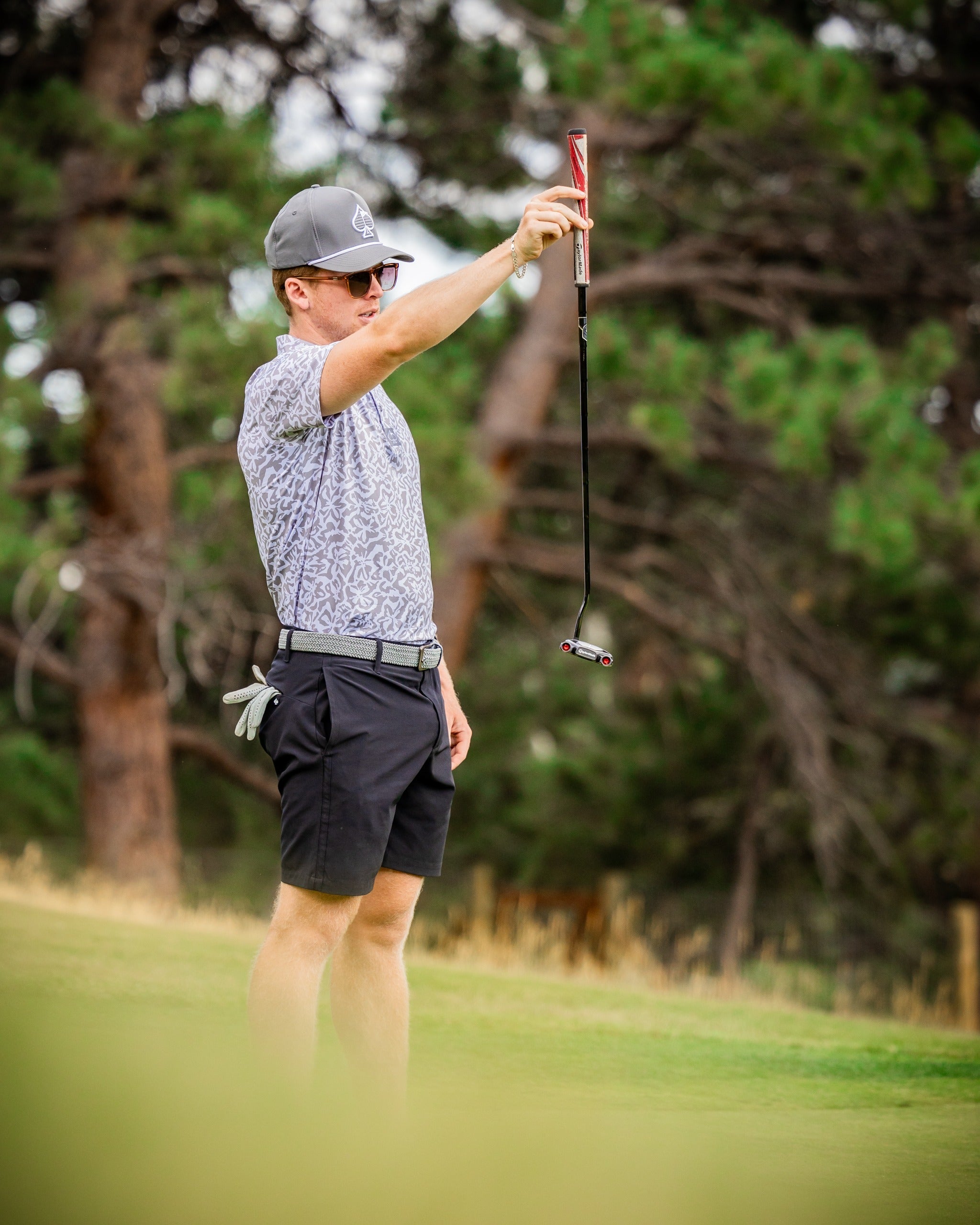 A golfer in a patterned shirt and cap holds a putter, focusing intently on the green in a natural setting.
