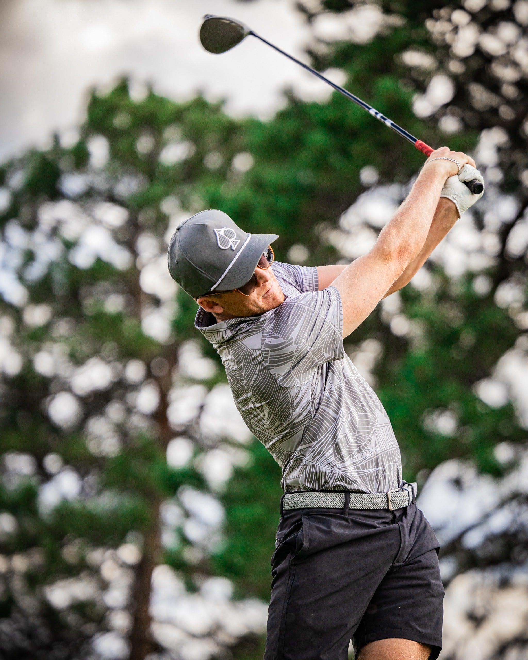 A golfer in a stylish palm-patterned shirt swings a driver on the course, showcasing bold golf fashion.