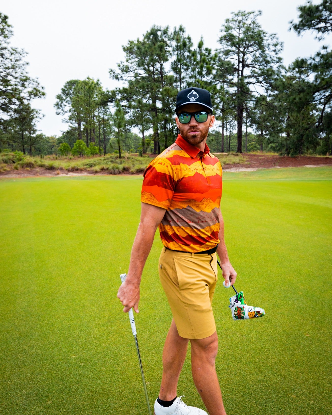 Bold golf shirt featuring a Yellowstone Montana sunset design, paired with stylish shorts and accessories on the course.