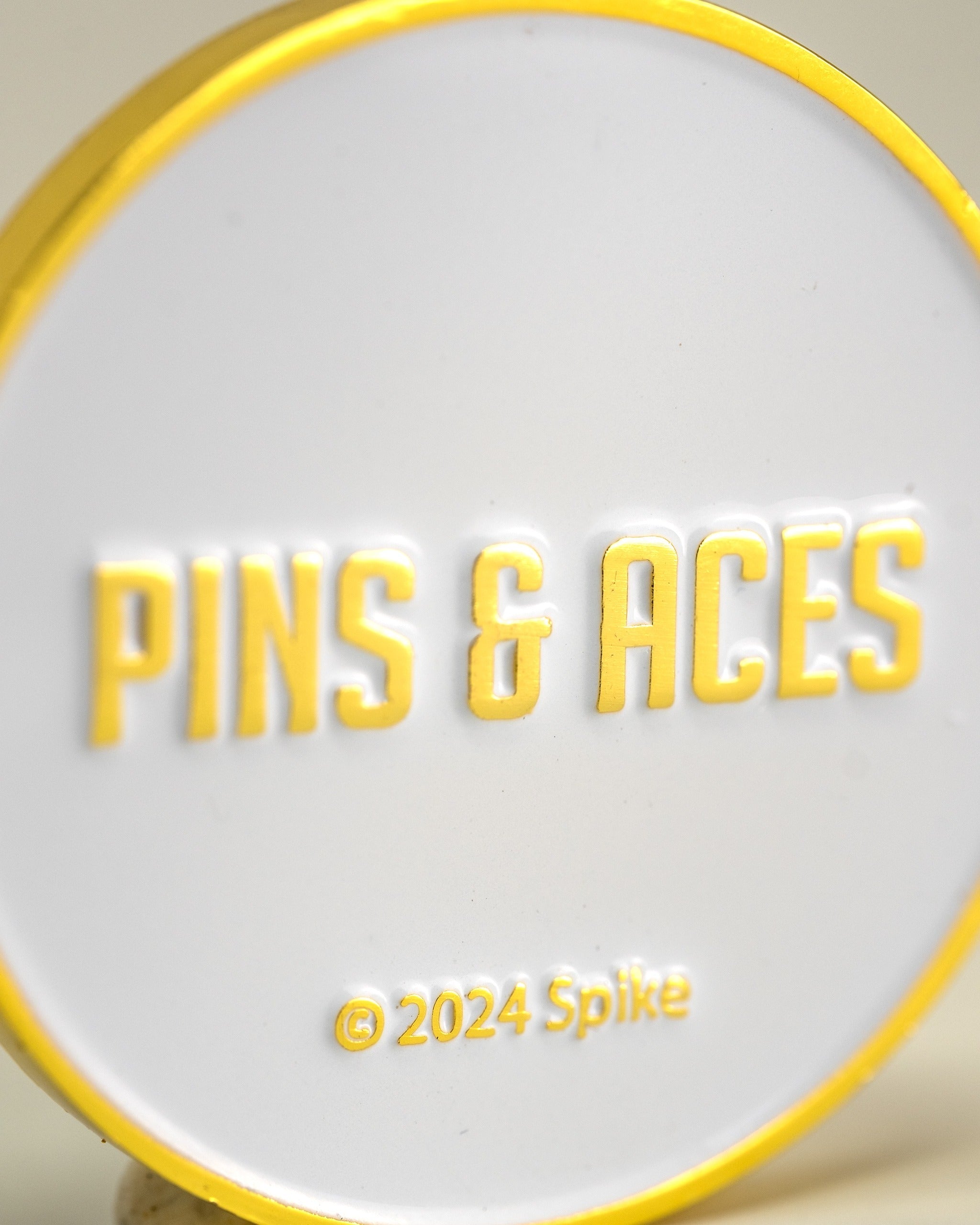 Yellowstone ball marker featuring a bold design with "Pins & Aces" text in yellow and white, perfect for golfers.