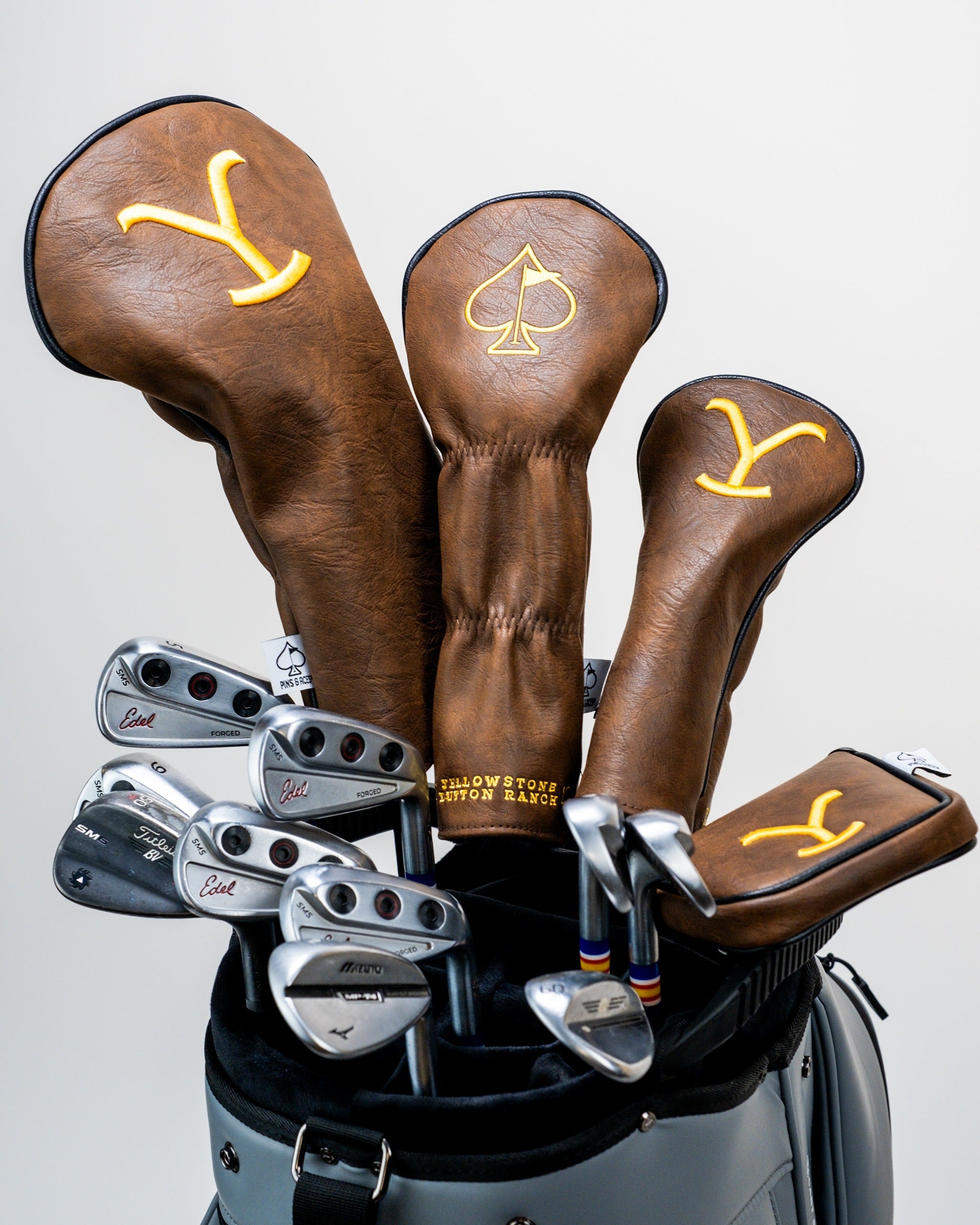 Yellowstone mallet putter cover in brown leather with yellow embroidery, displayed among golf clubs in a bag.