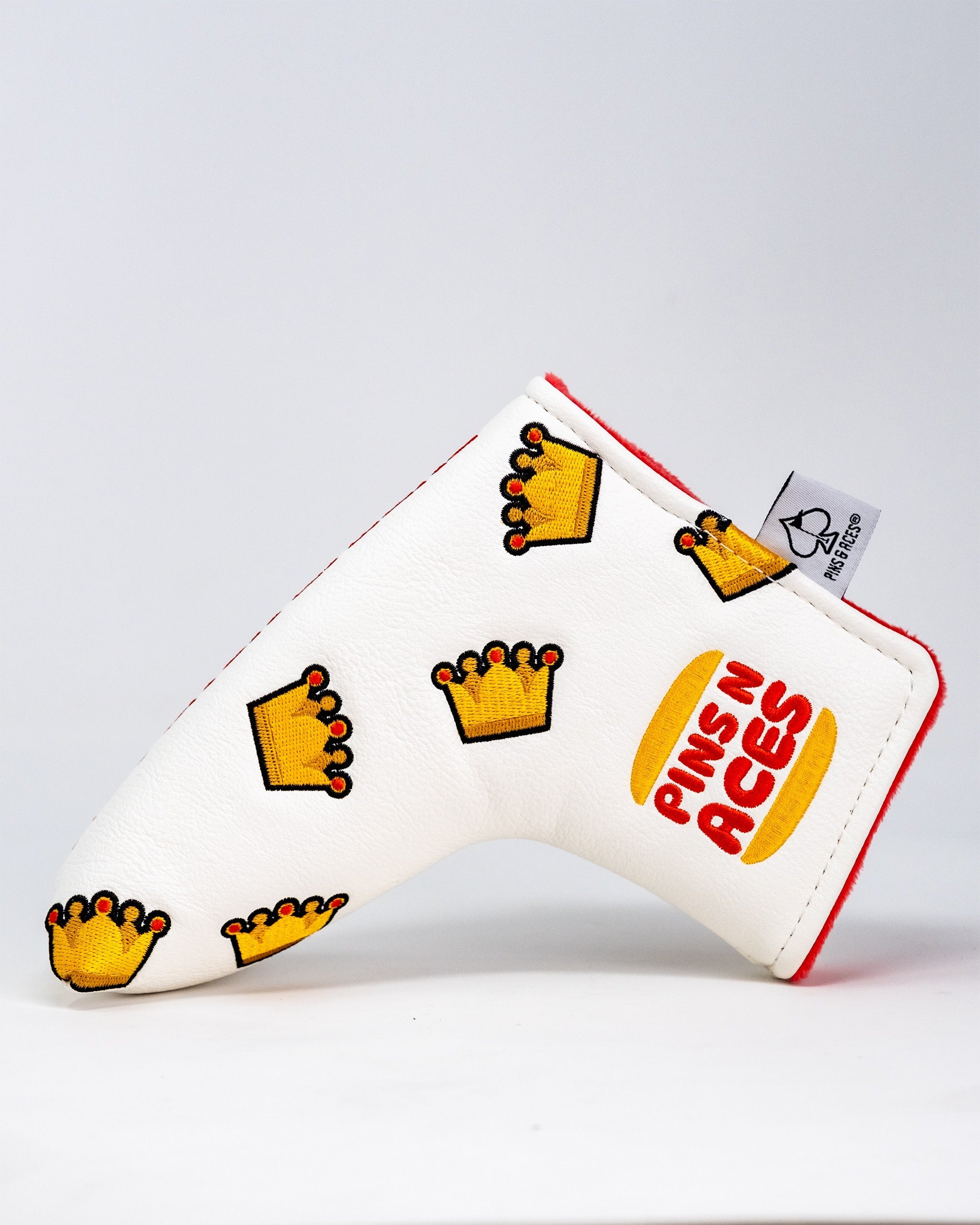 White blade putter cover featuring colorful crown designs and the Pins N Aces logo, perfect for stylish golfers.