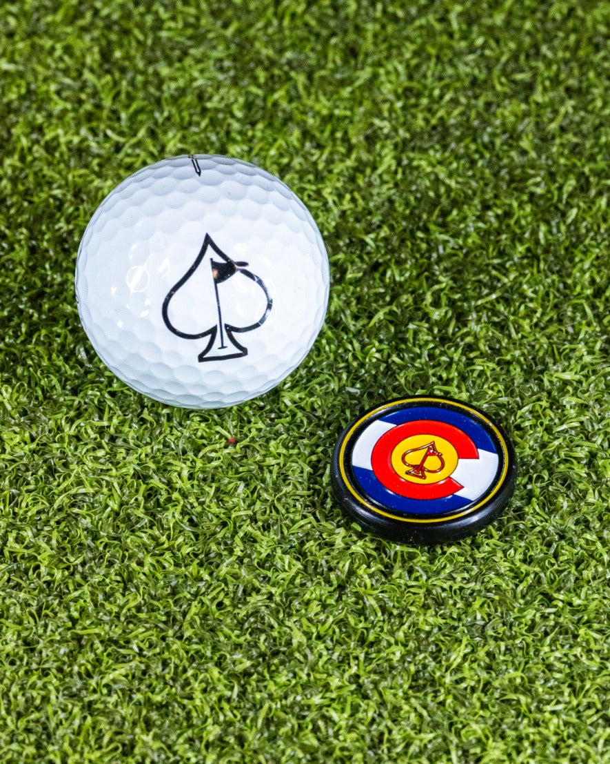 Pop Out Medallion Ball Marker featuring Colorado design next to a golf ball with an ace of spades logo on grass.