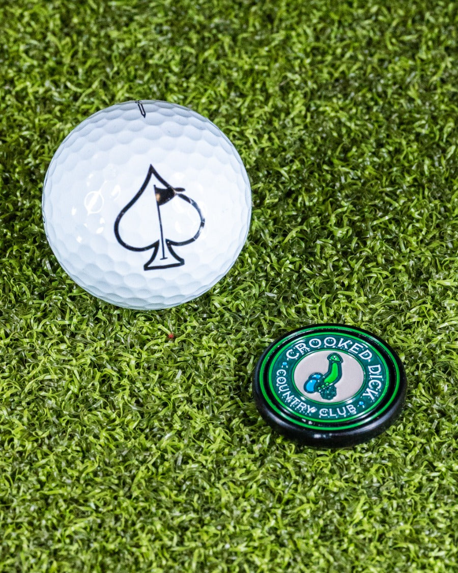 Pop Out Medallion Ball Marker featuring Crooked Dick design next to a golf ball on a green turf background.