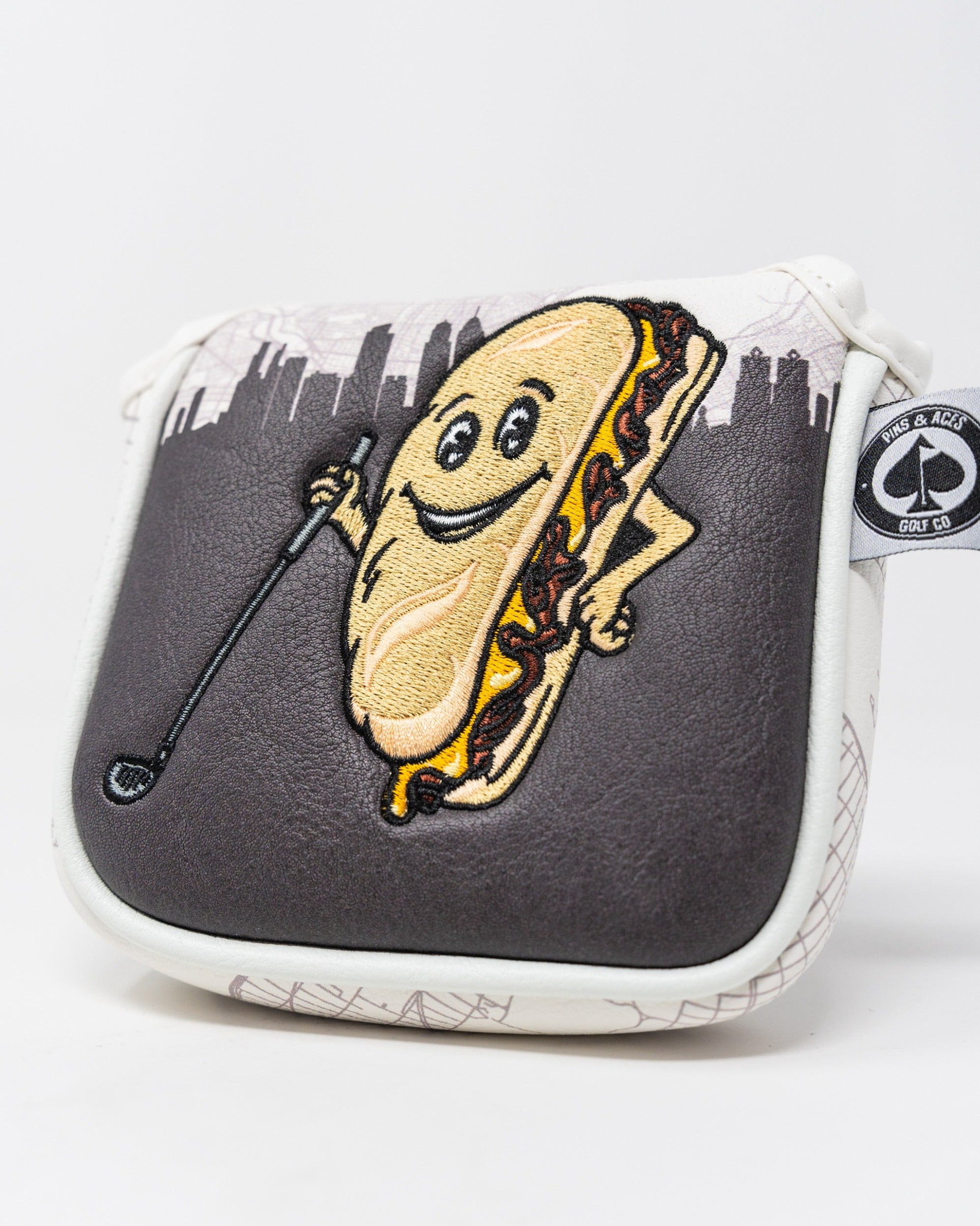 Whiz Wit mallet cover featuring a playful hot dog character holding a golf club against a city skyline background.