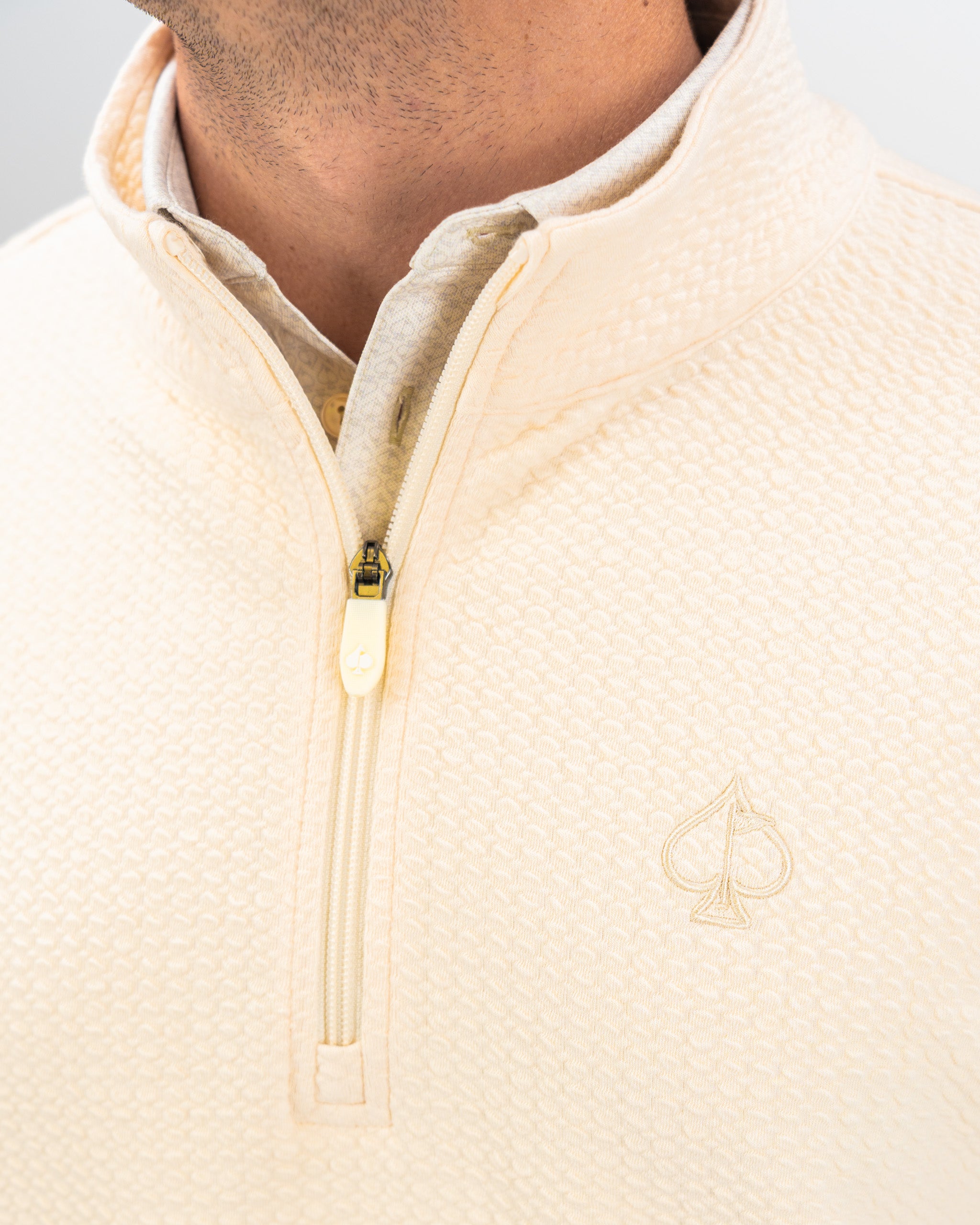 Cream waffle knit pullover with a half-zip collar and embroidered logo, designed for stylish comfort on the golf course.