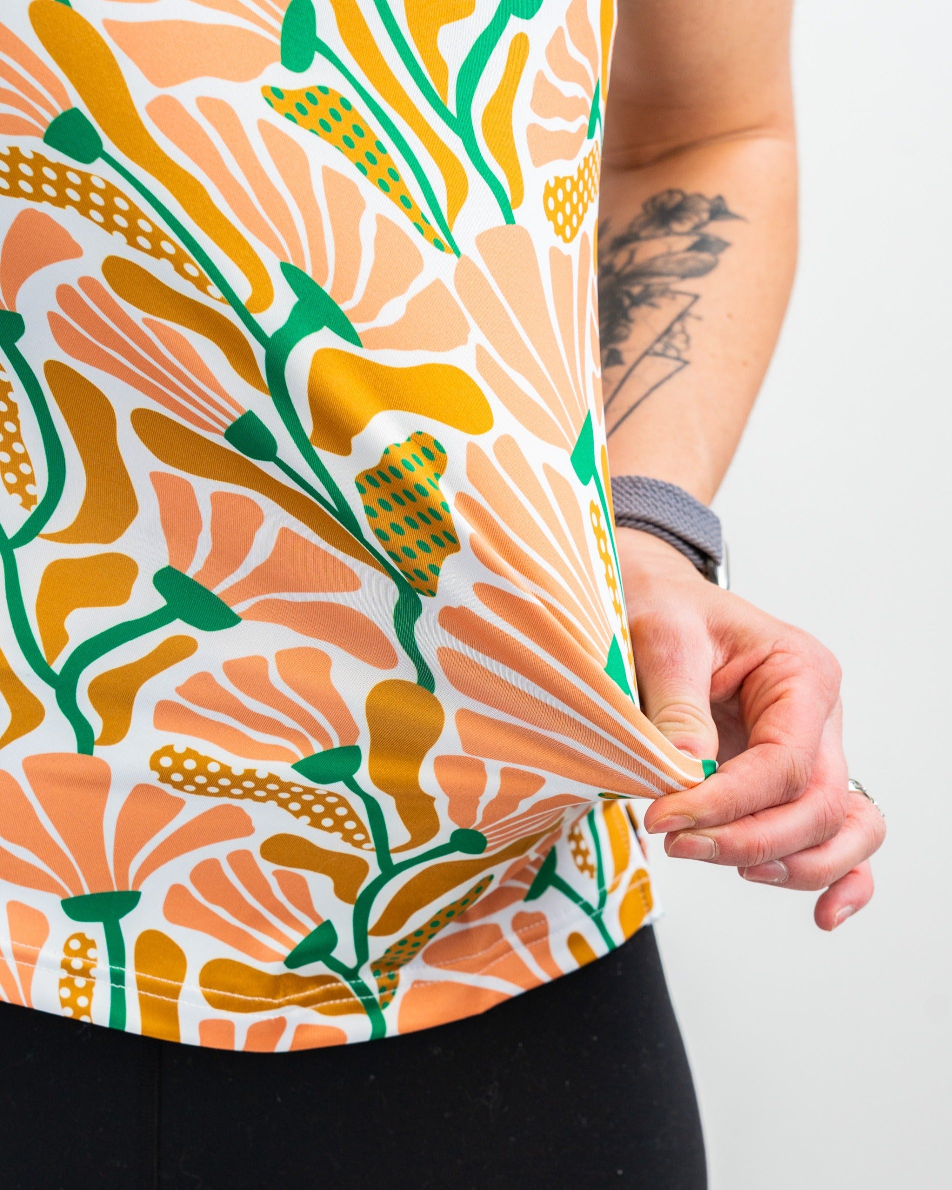 Women's Garden Party Spritz top featuring a vibrant floral pattern in orange, green, and yellow hues, styled with black leggings.