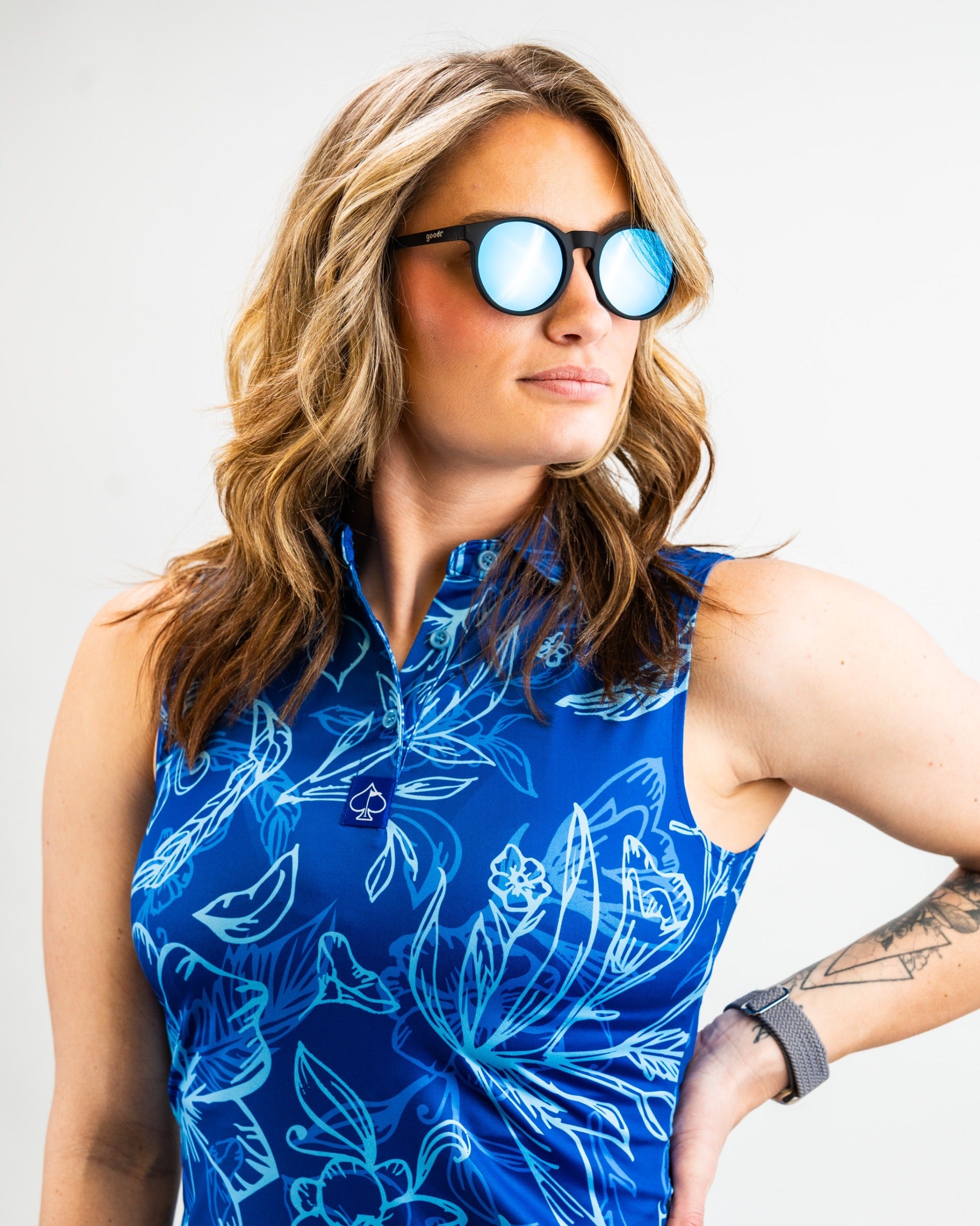 Stylish woman in a blue floral golf polo, wearing reflective sunglasses, showcasing bold golf fashion for women.