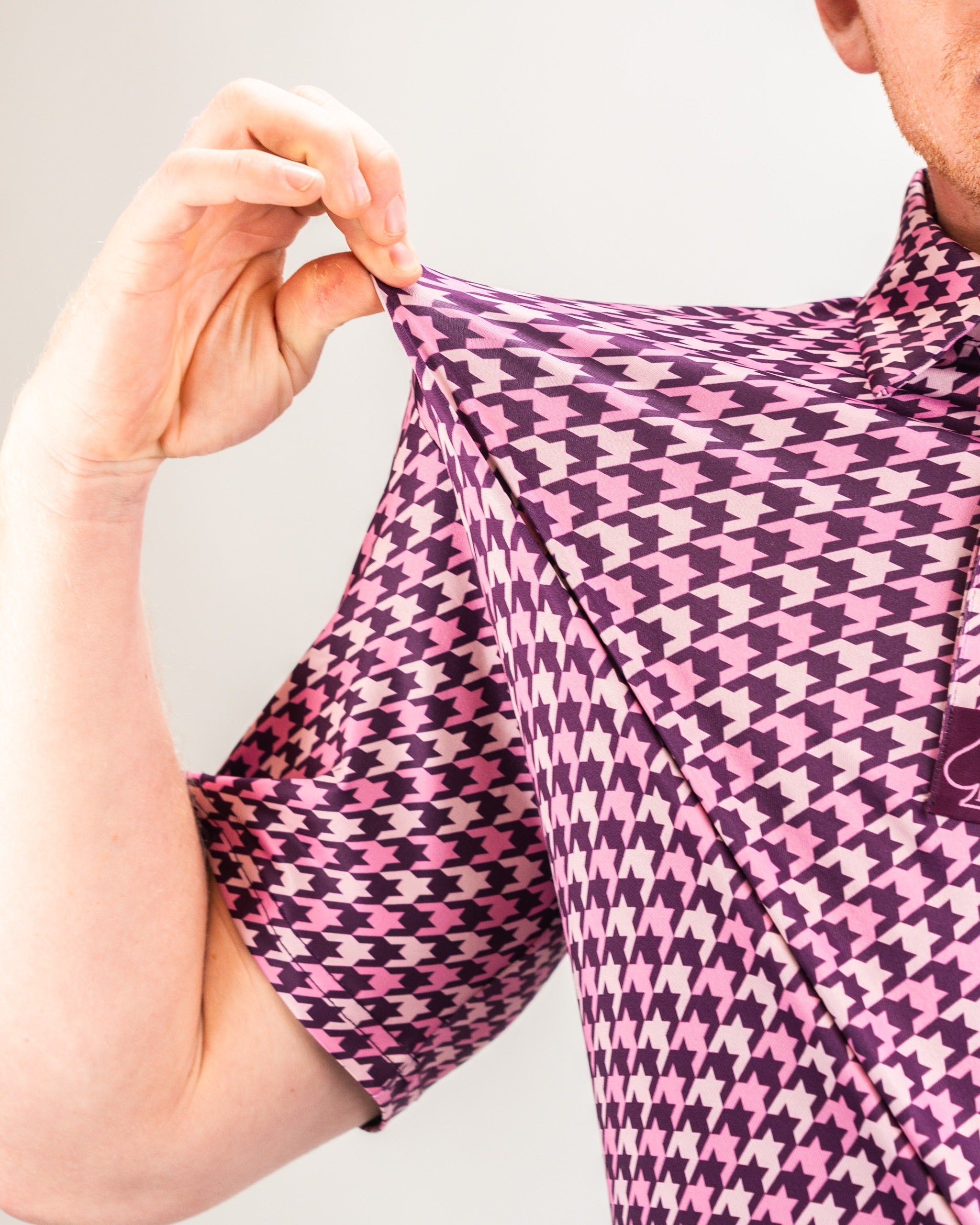 Bold houndstooth golf shirt in raspberry shades, showcasing unique pattern and stylish collar for standout performance on the course.