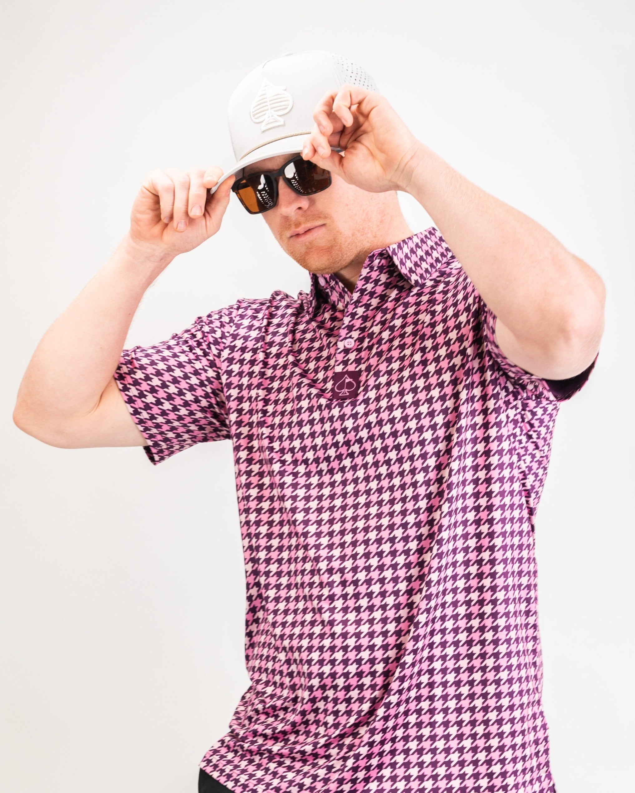 Bold houndstooth golf shirt in raspberry pink, worn with sunglasses and a cap, perfect for stylish golfers on the course.