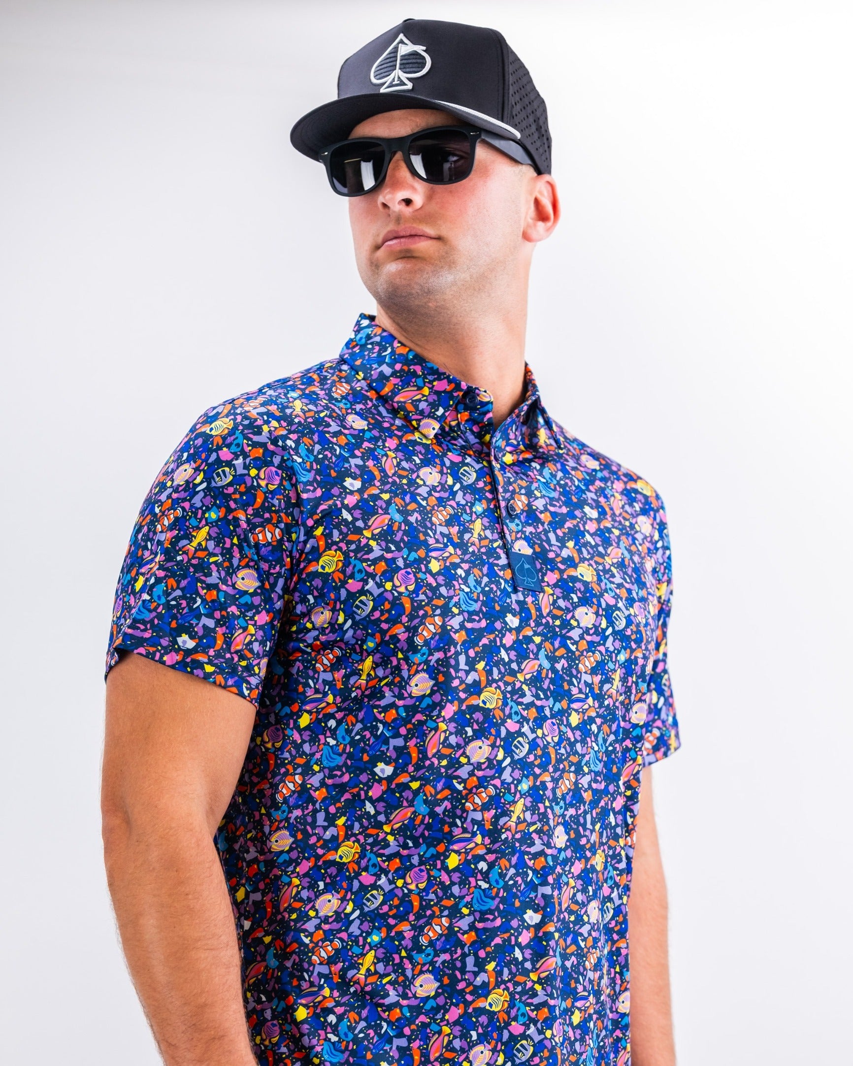 Bold tropical print short-sleeve shirt worn by a man with sunglasses and a black cap, showcasing vibrant colors and patterns.