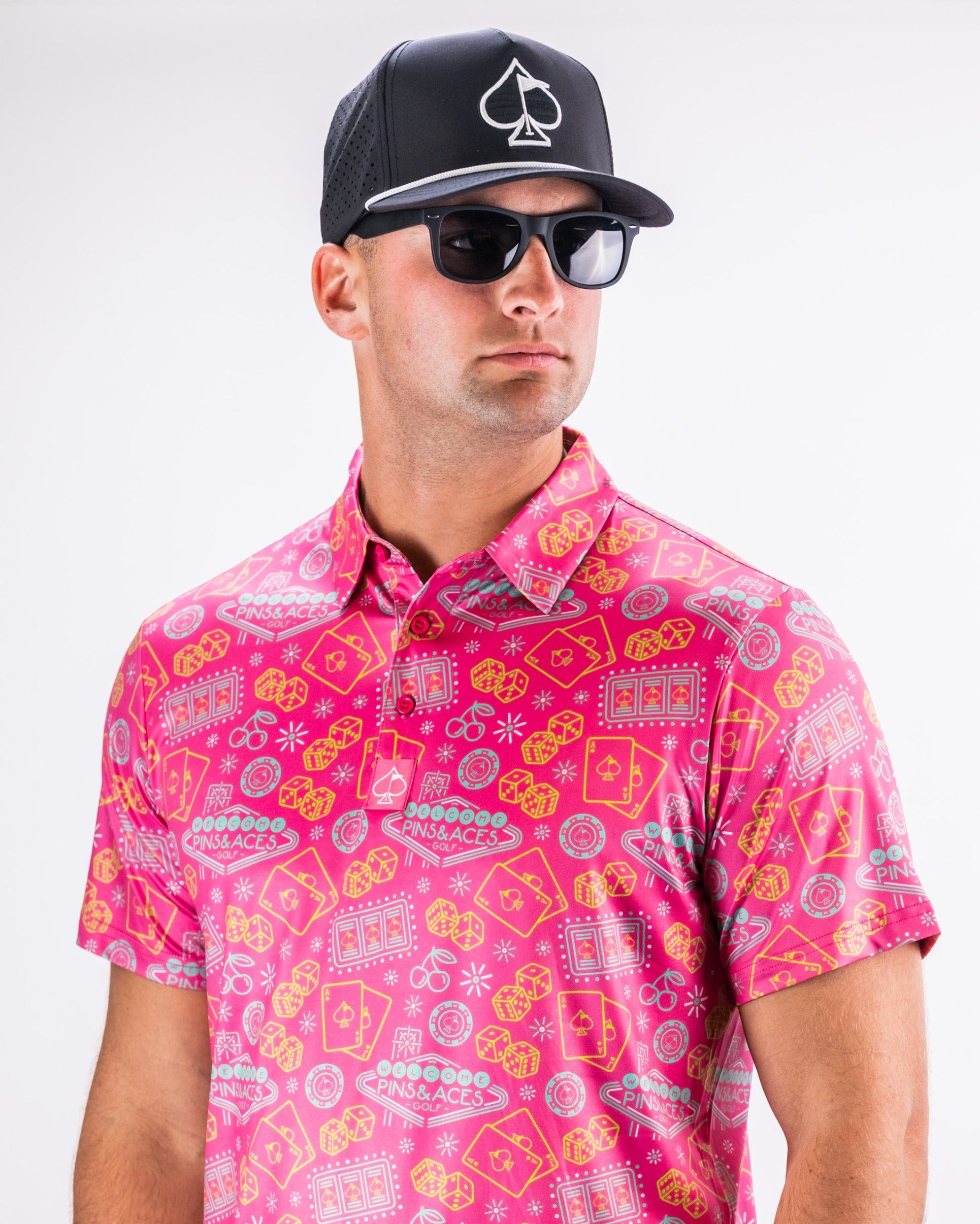 Bold fuchsia golf polo featuring playful patterns, paired with a black cap and sunglasses for a stylish on-course look.