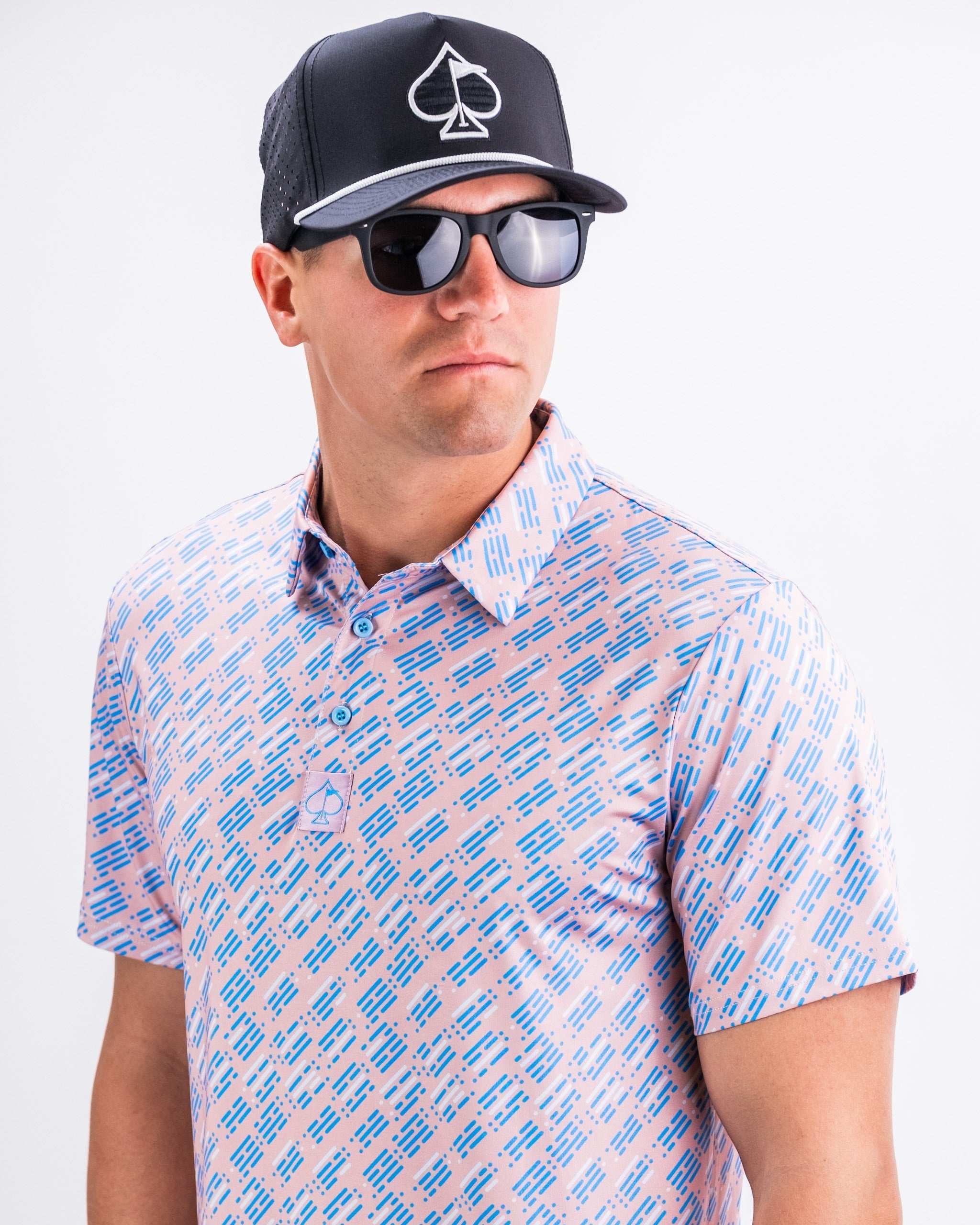 Stylish golfer wearing a pink patterned polo shirt and a black cap, showcasing bold golf fashion for standout performance.