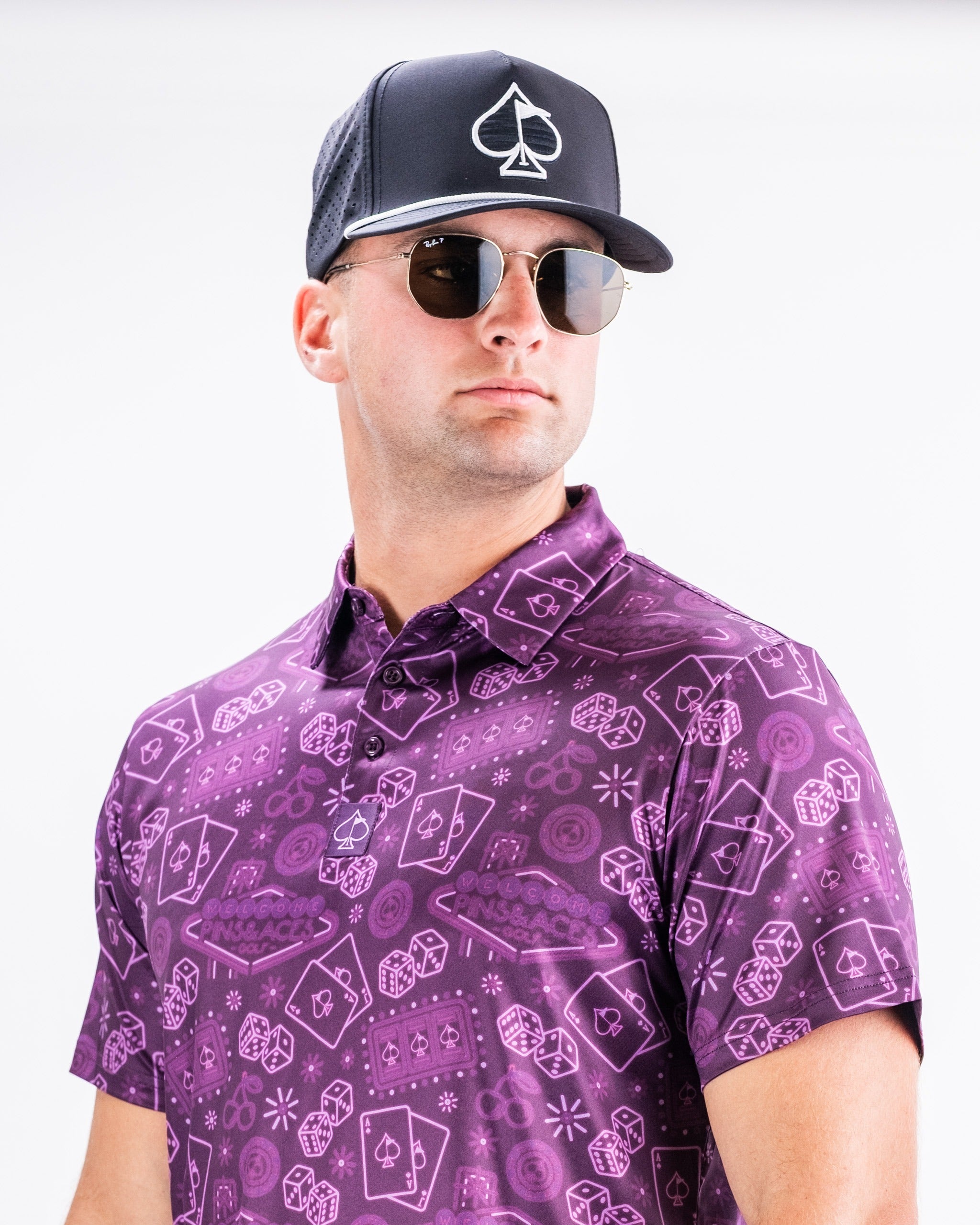 Bold purple golf polo featuring unique patterns, paired with a black cap and sunglasses for a stylish on-course look.