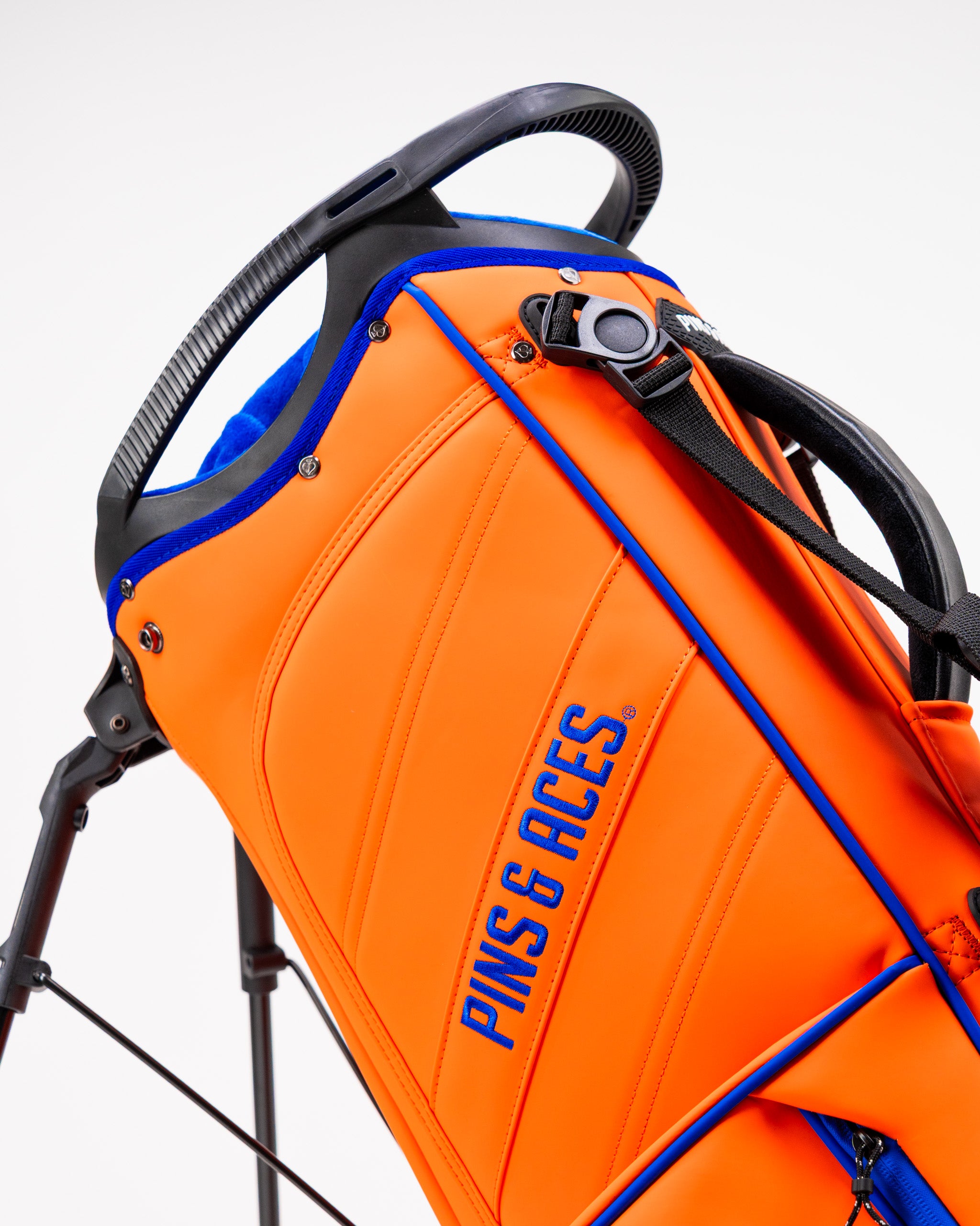Bright orange Player Preferred golf bag featuring a sleek design and the Pins & Aces logo, ideal for stylish golfers.