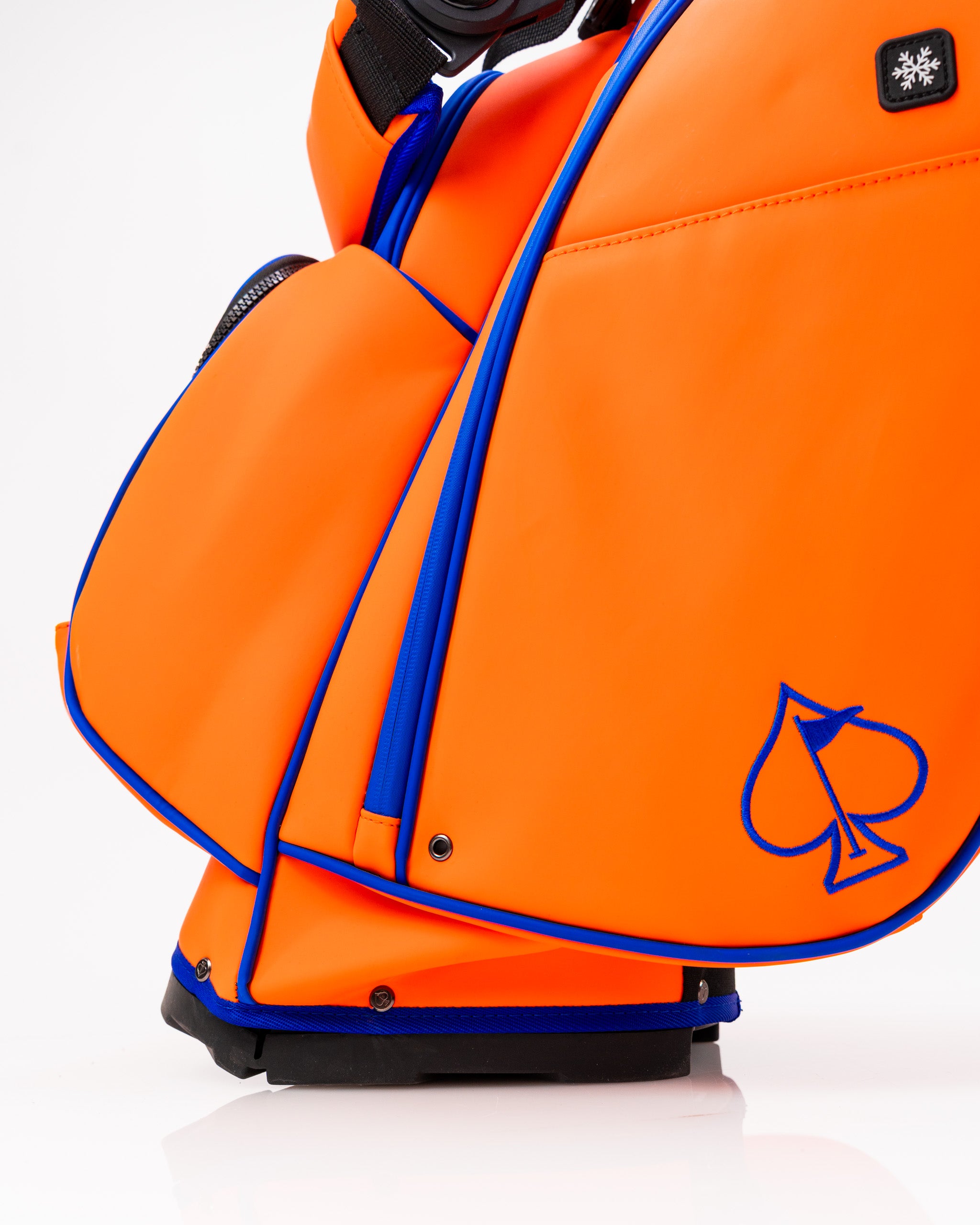 Bold orange golf bag with blue accents, featuring a spade logo and multiple pockets for storage. Ideal for standout golfers.