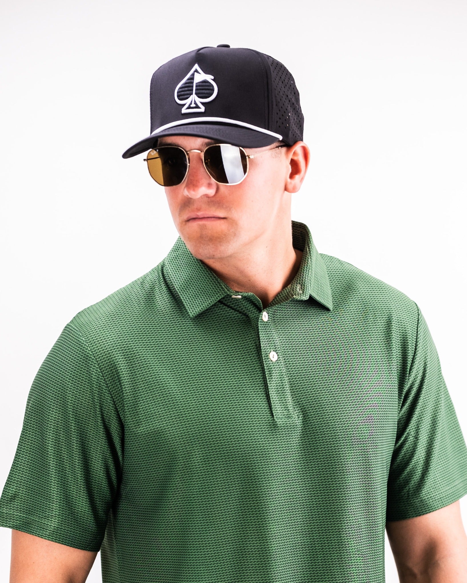Man wearing a green Player Preferred Polo with a textured pattern, black cap, and sunglasses, showcasing a stylish golf look.
