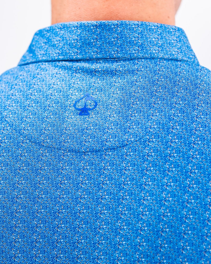 Back view of a blue Player Preferred Polo featuring a cosmic swirl pattern and a small logo on the collar.