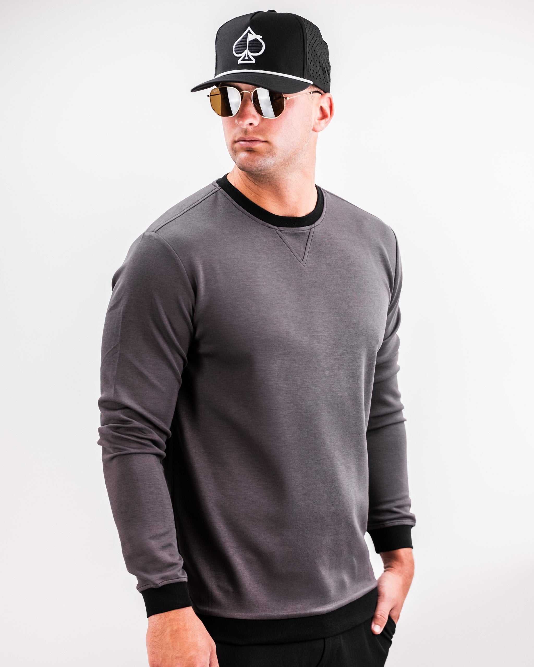 Slate grey crewneck sweatshirt with a fitted design, worn by a model in a black cap and sunglasses, showcasing a stylish golf look.