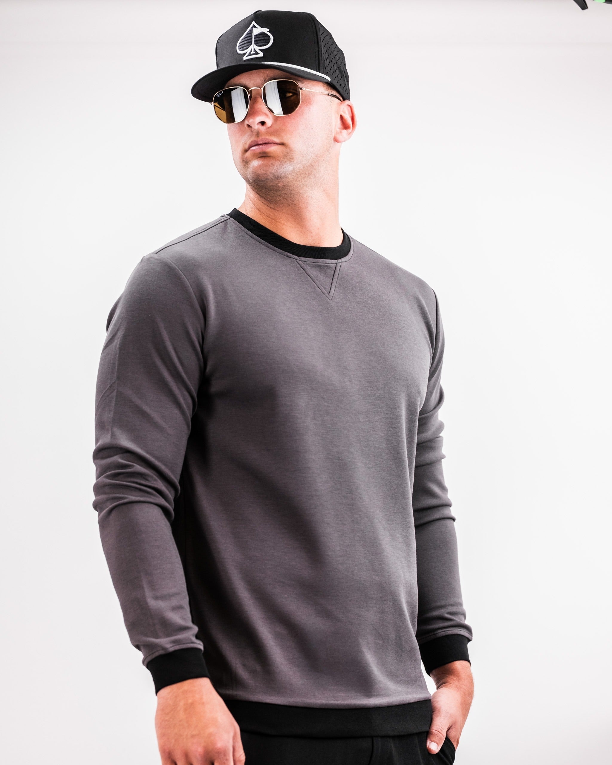 Slate grey crewneck sweatshirt with black trim, worn by a model in sunglasses and a cap, showcasing a stylish golf look.