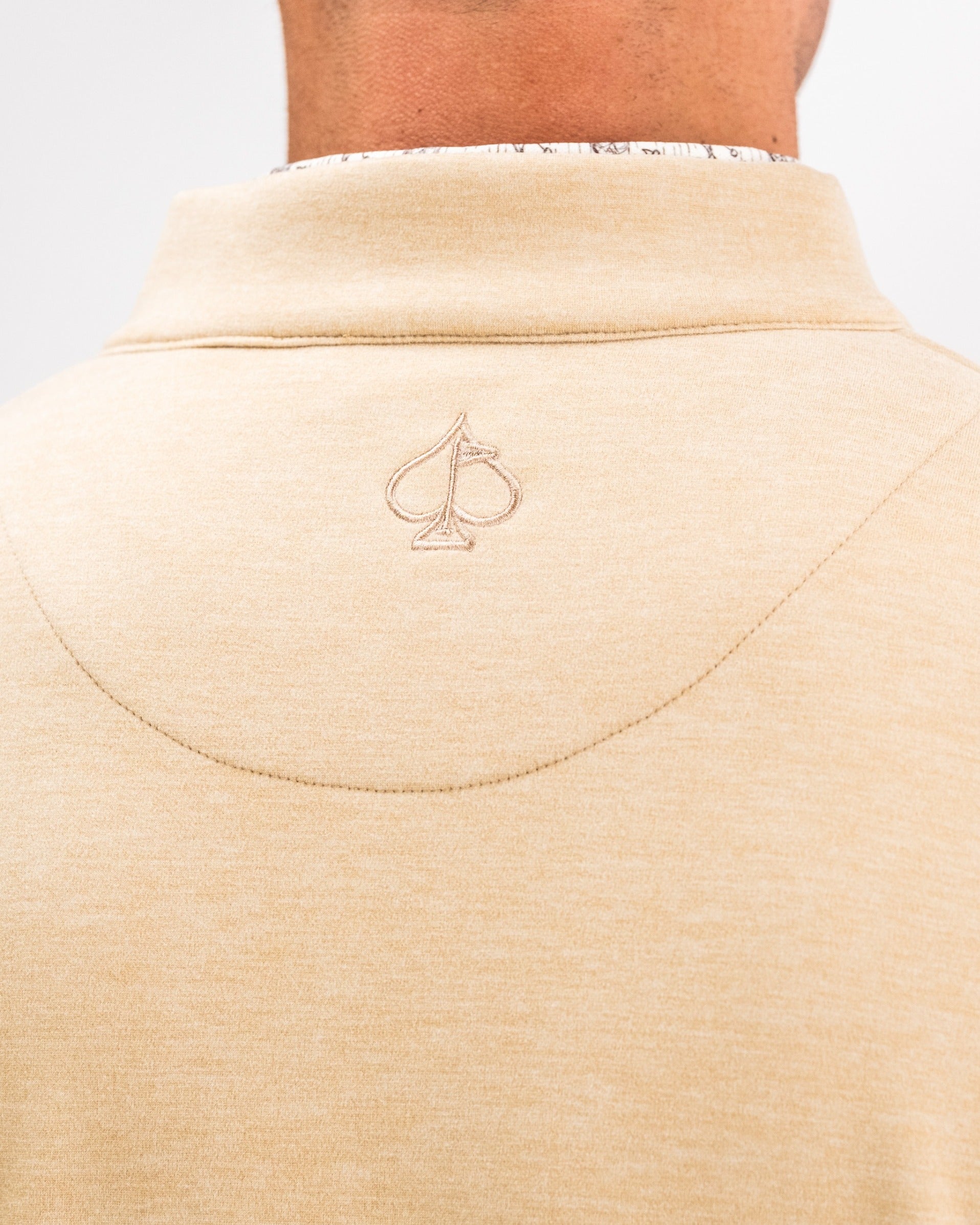 Close-up of the back of a sand-colored Player Preferred pullover featuring an embroidered spade logo.