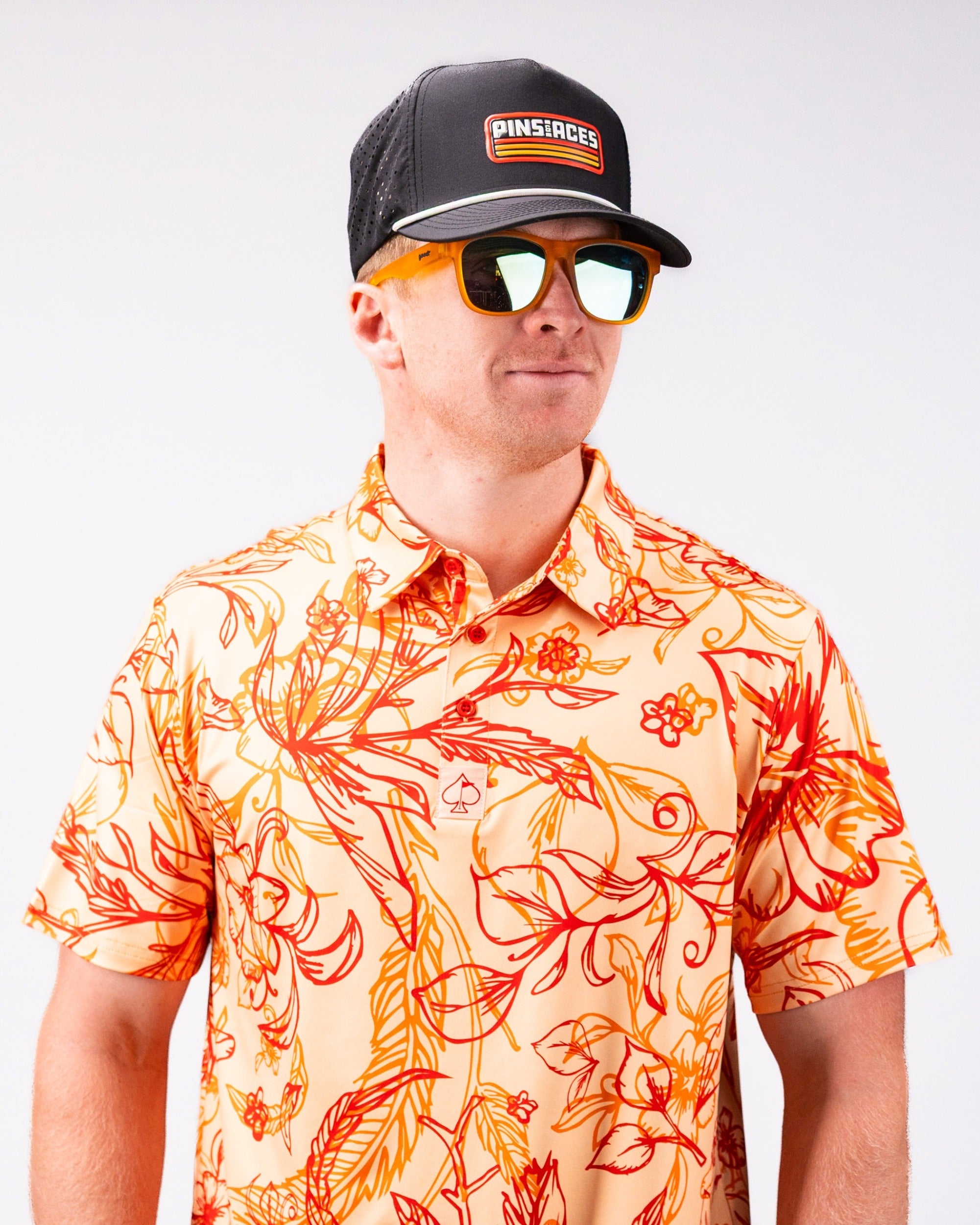 Bold floral print shirt in warm tones paired with a black cap and reflective sunglasses, perfect for stylish golf outings.