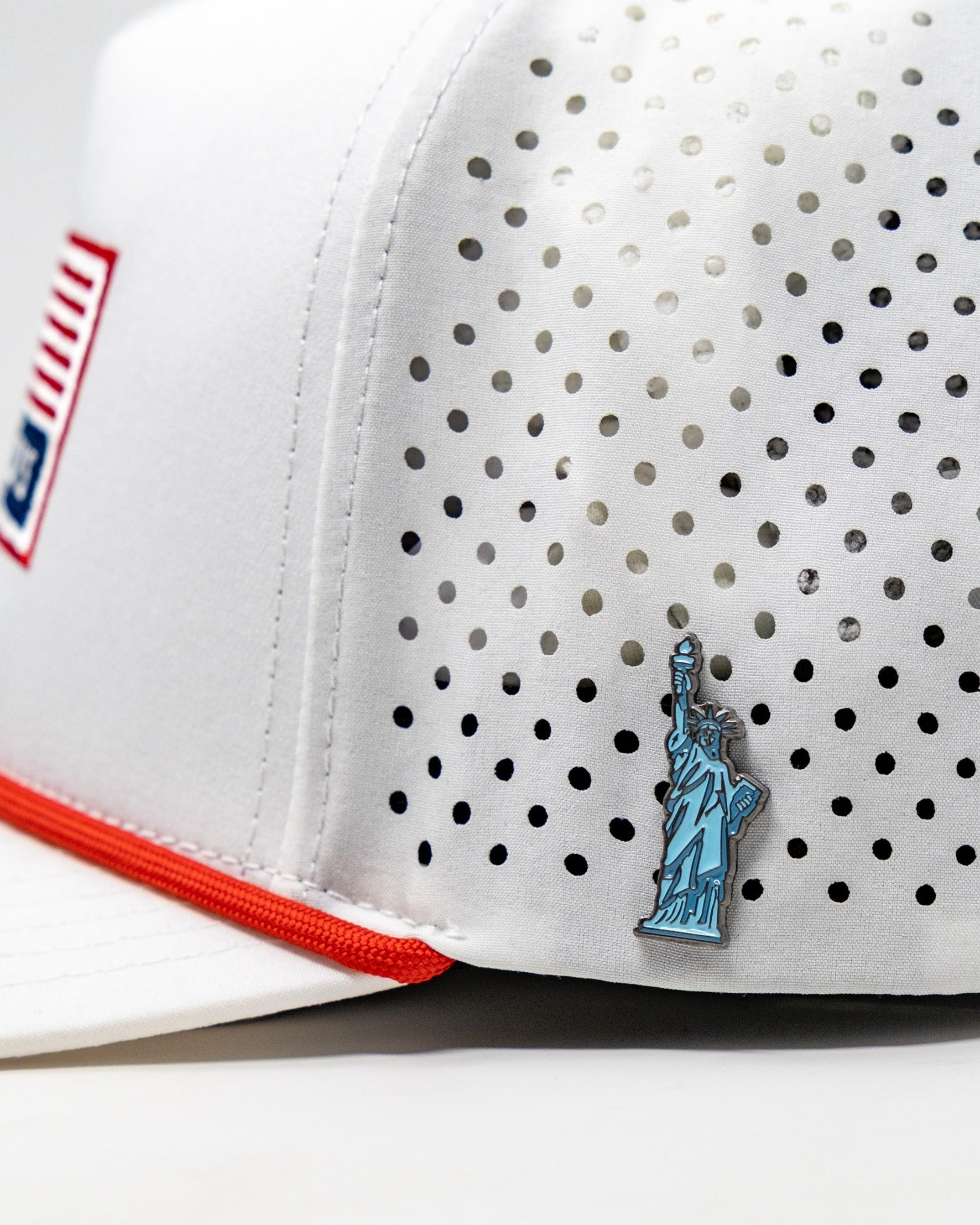 Perforated white rope hat featuring a blue Statue of Liberty emblem and red accents, perfect for patriotic golfers.