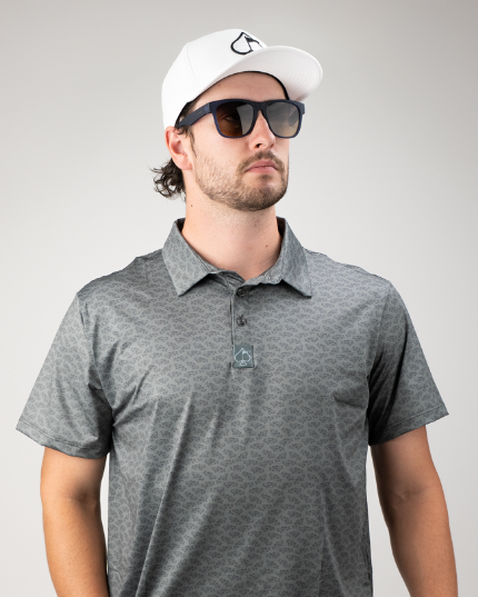 Stylish golfer wearing a patterned polo shirt and a white cap, showcasing bold golf apparel for a standout look on the course.