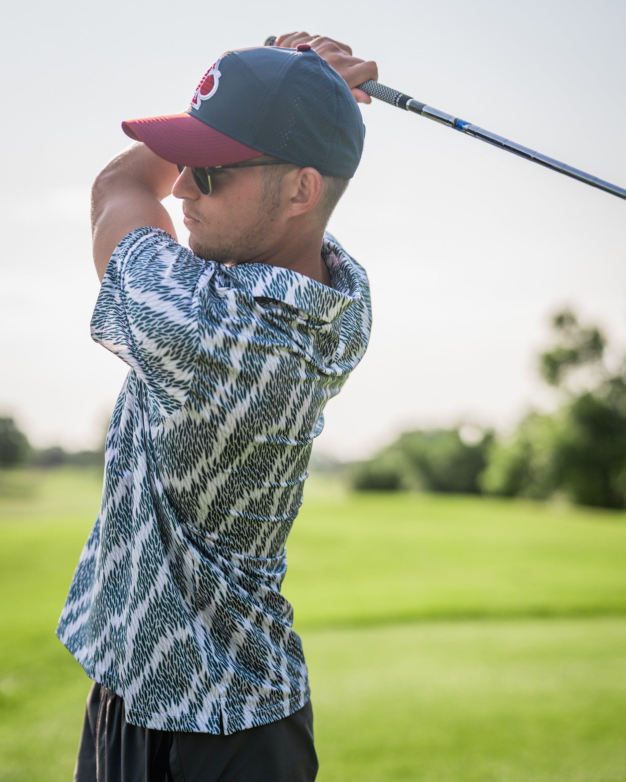 A golfer in a stylish striped shirt and cap prepares to swing on a sunny golf course, showcasing bold apparel.