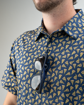 A close-up of a man wearing a pizza-patterned shirt, with sunglasses hanging from the collar, showcasing a fun, casual style.