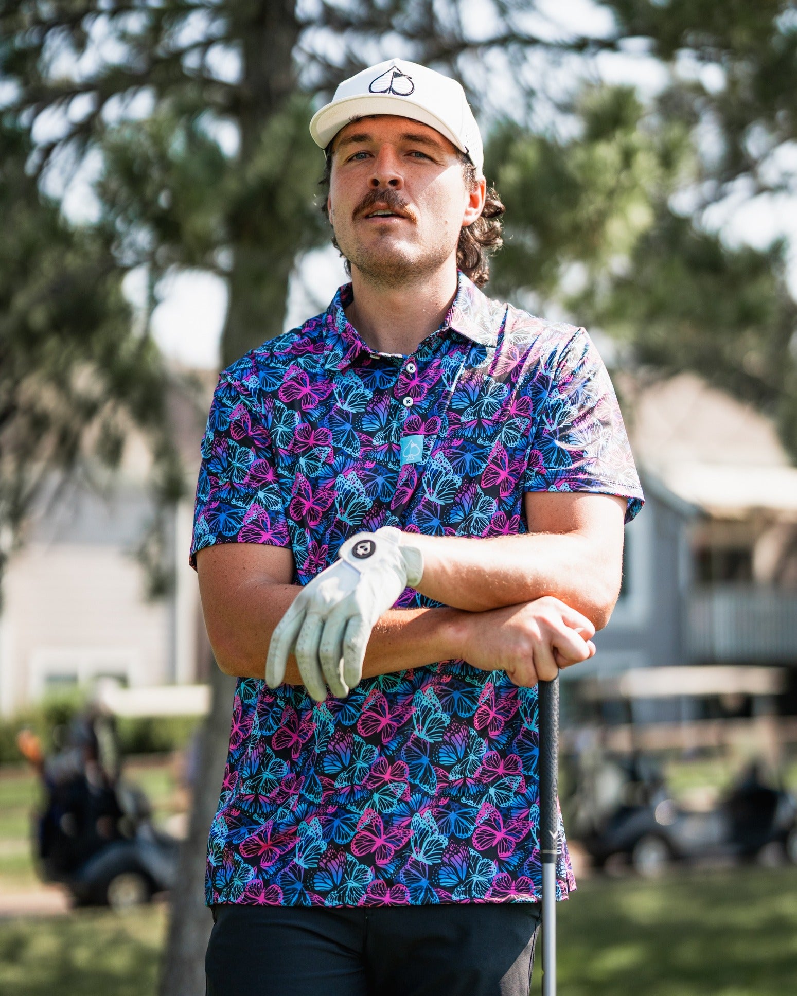 A golfer stands confidently on the course wearing a vibrant butterfly-patterned polo shirt, showcasing bold style.
