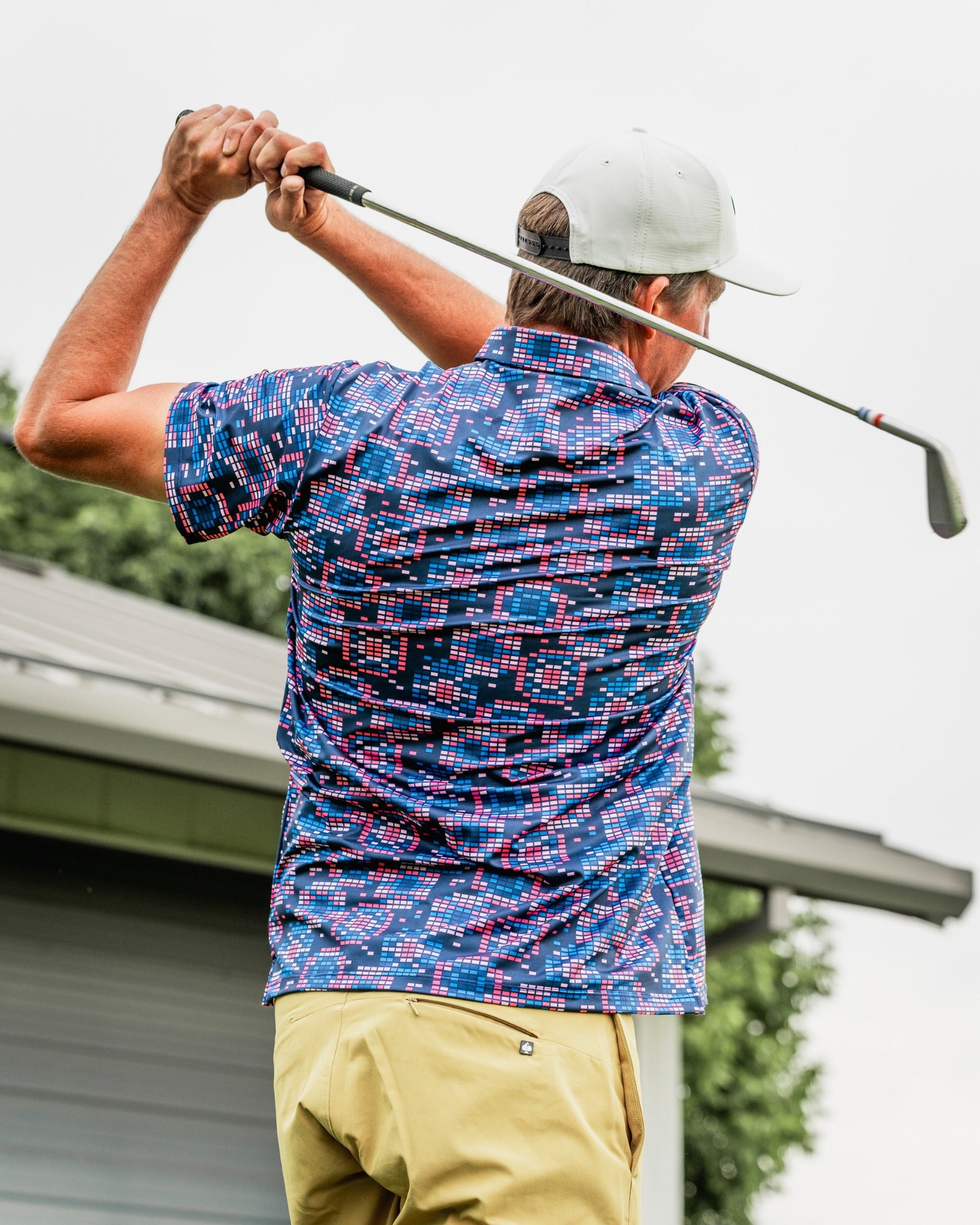 A golfer swings a club while wearing a Tetrafloral Dark patterned shirt, showcasing bold colors and a unique design.