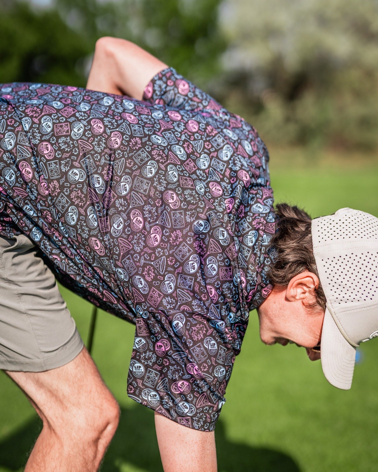 A golfer in a colorful patterned shirt bends down on the course, showcasing a playful and bold style.