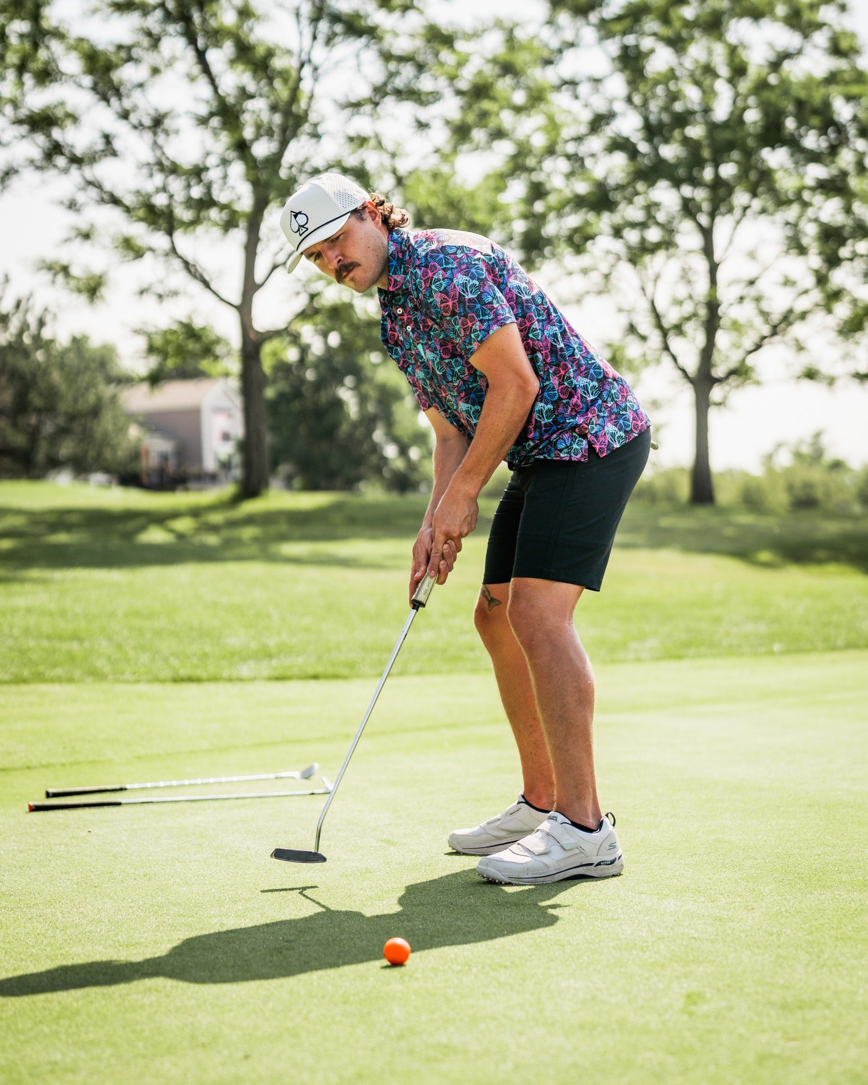 Man in a vibrant floral golf shirt and shorts putts on the green, showcasing bold golf apparel in action.