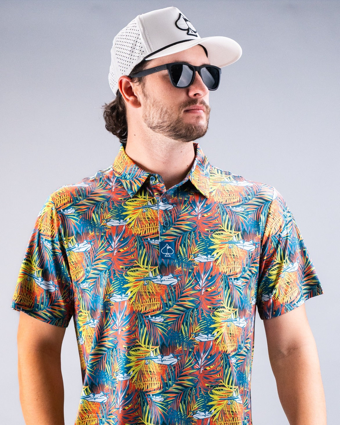 Colorful Margaritaville Bama Breeze polo shirt featuring a tropical print, worn by a man with sunglasses and a cap.