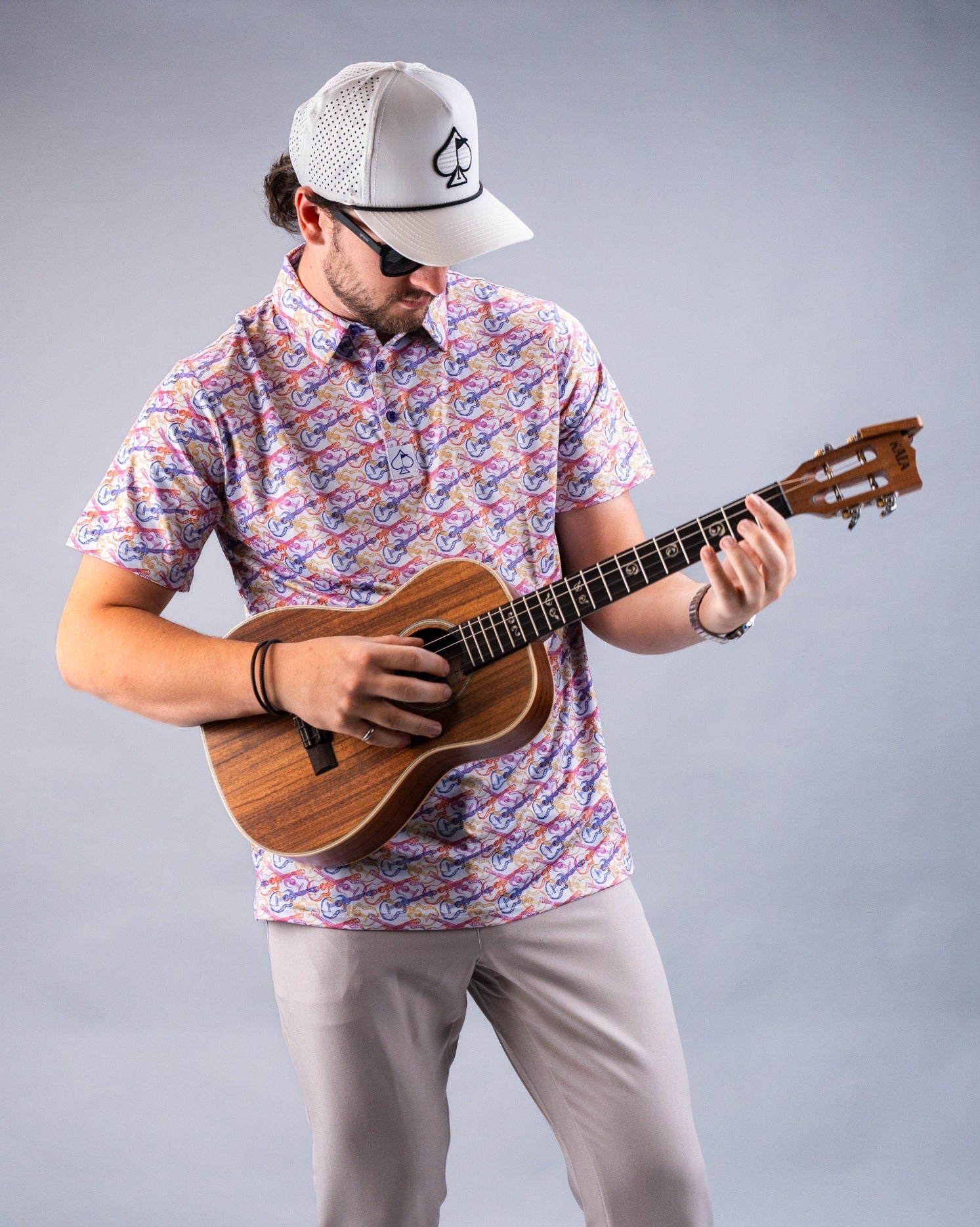 A man plays a ukulele while wearing a colorful Margaritaville shirt and a white cap, showcasing a relaxed, beach-inspired vibe.