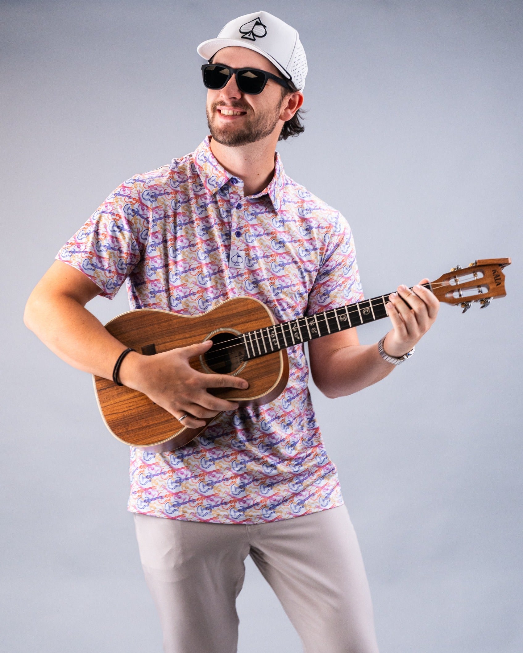 Man wearing a colorful Margaritaville shirt and sunglasses, playing a ukulele with a relaxed smile.