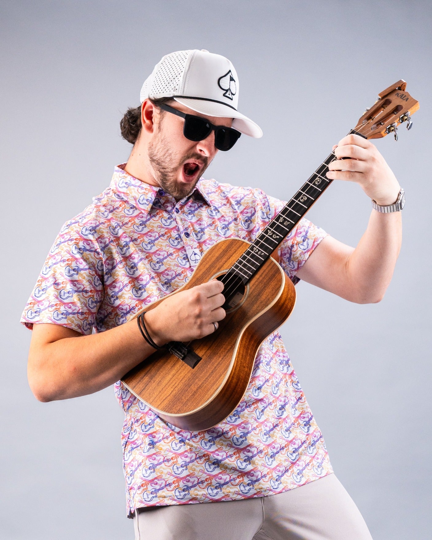 A man in a colorful shirt and sunglasses passionately plays a ukulele, embodying a fun, relaxed vibe.