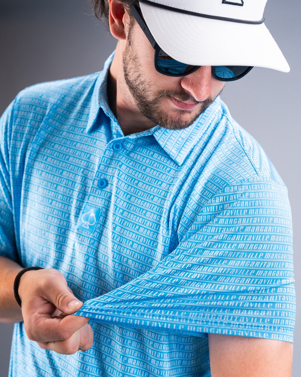 Model showcasing the Margaritaville Rendezvous polo shirt in blue, featuring a bold logo pattern and stylish sunglasses.