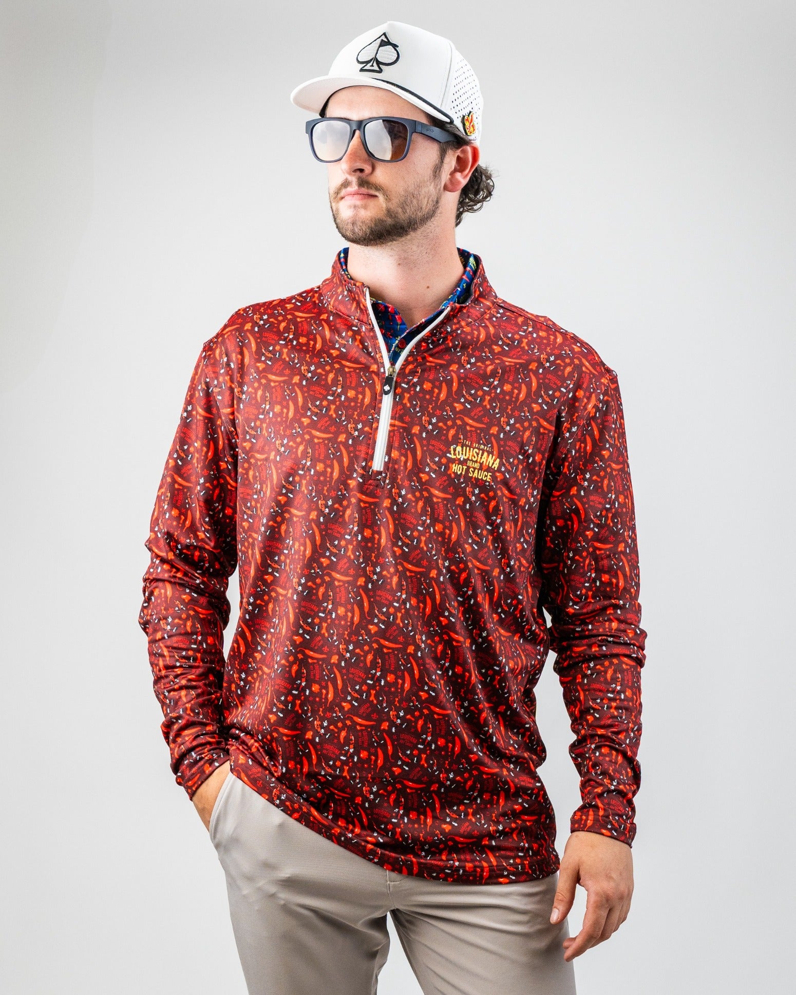 Man in red Louisiana Hot Sauce golf pullover with abstract print, zip collar, and embroidered logo, wearing sunglasses and...