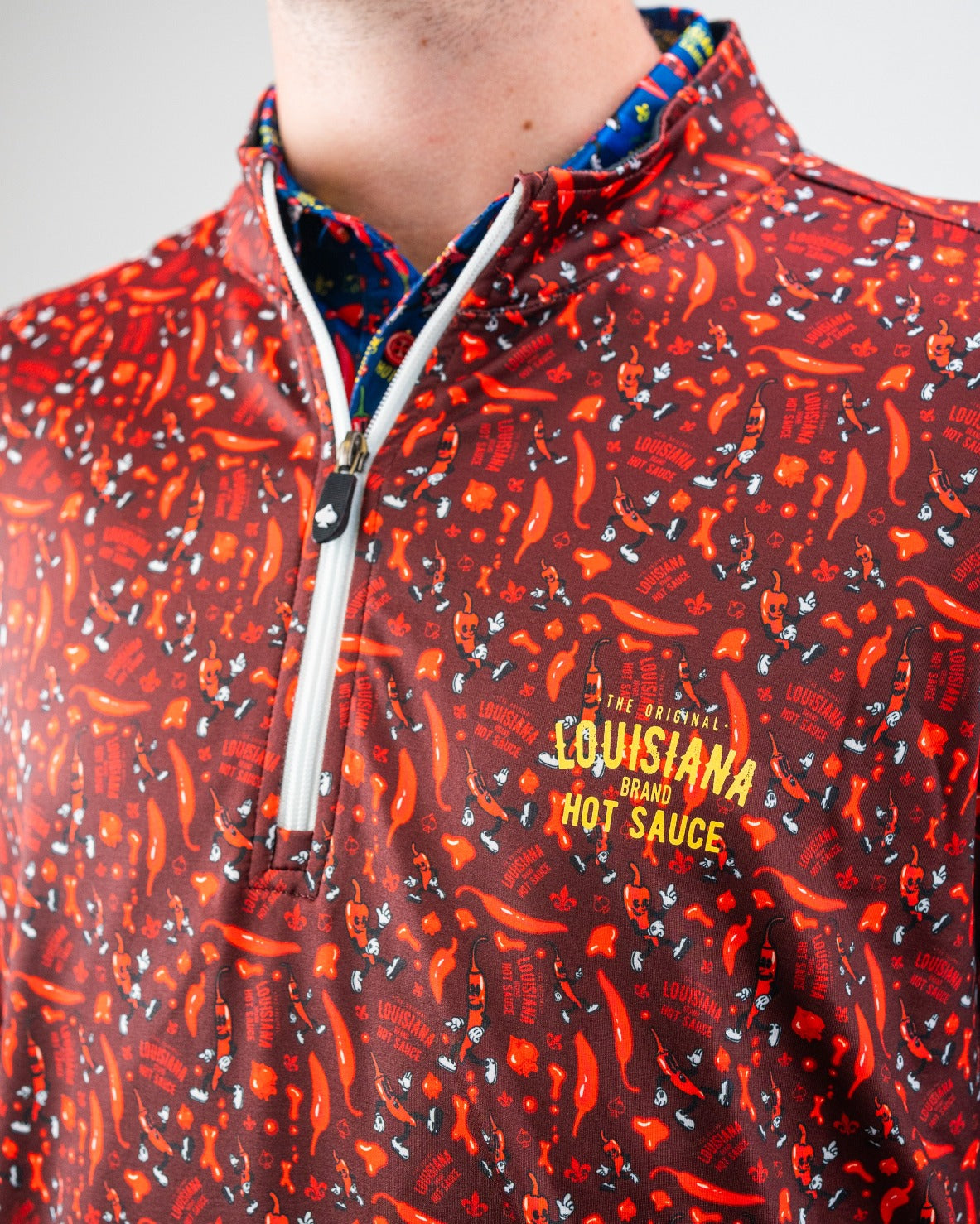 Close-up of a bold red golf jacket with chili pepper and hot sauce graphics, featuring "Louisiana Hot Sauce" logo in yellow.