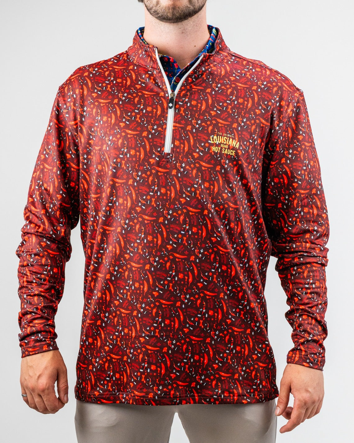 Bold red and black Louisiana Hot Sauce golf pullover with a quarter-zip, vibrant chili pepper pattern, and logo on chest.