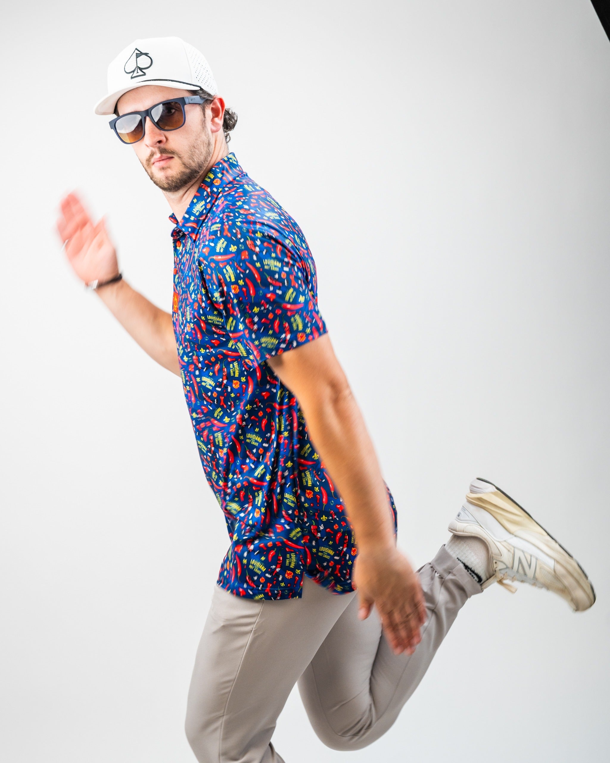 A man models a vibrant Louisiana Hot Sauce polo featuring a dancing peppers design, paired with light pants and sunglasses.