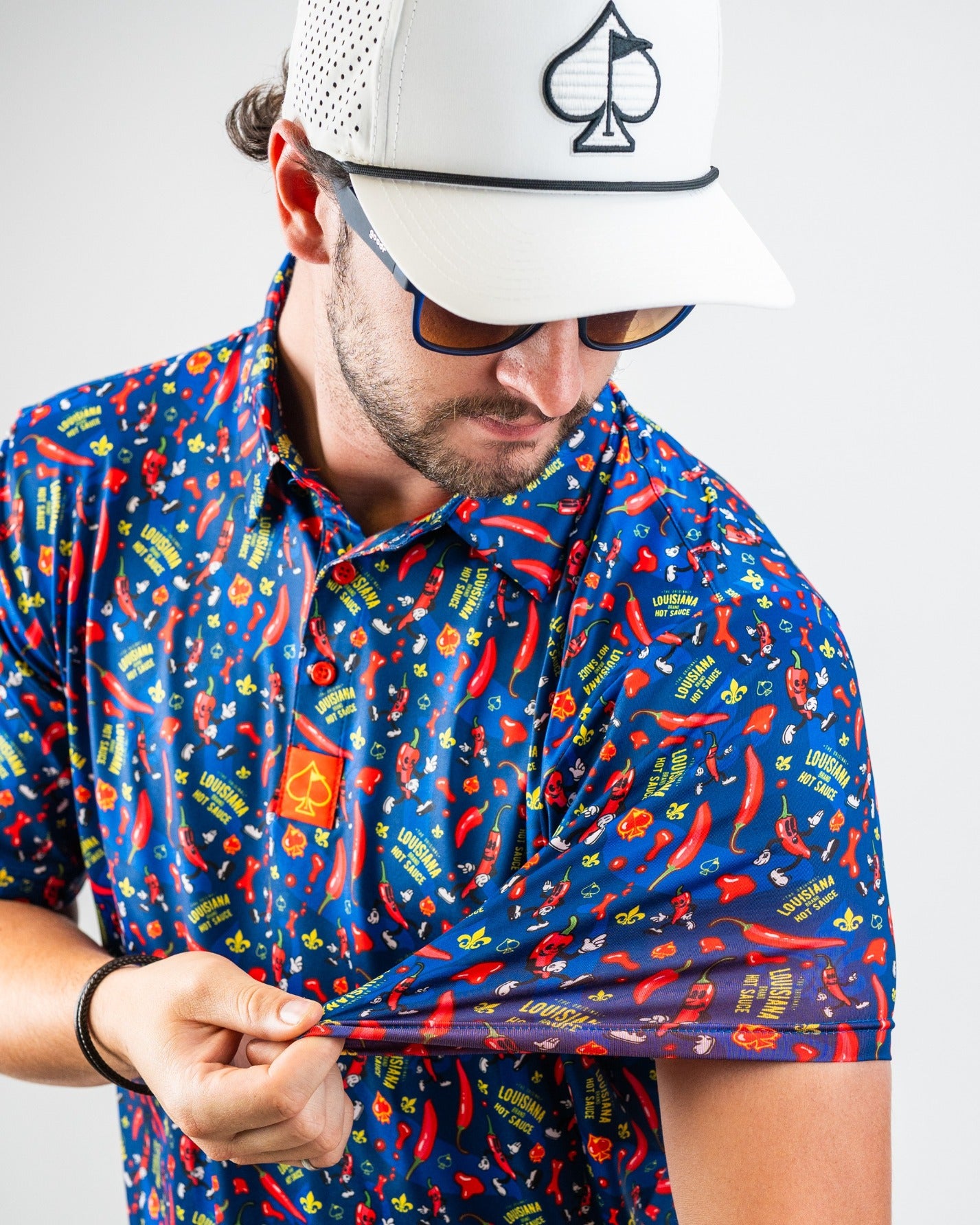 Bold blue golf shirt with red hot chili peppers, yellow Louisiana hot sauce, and spicy graphics for standing out on the co...