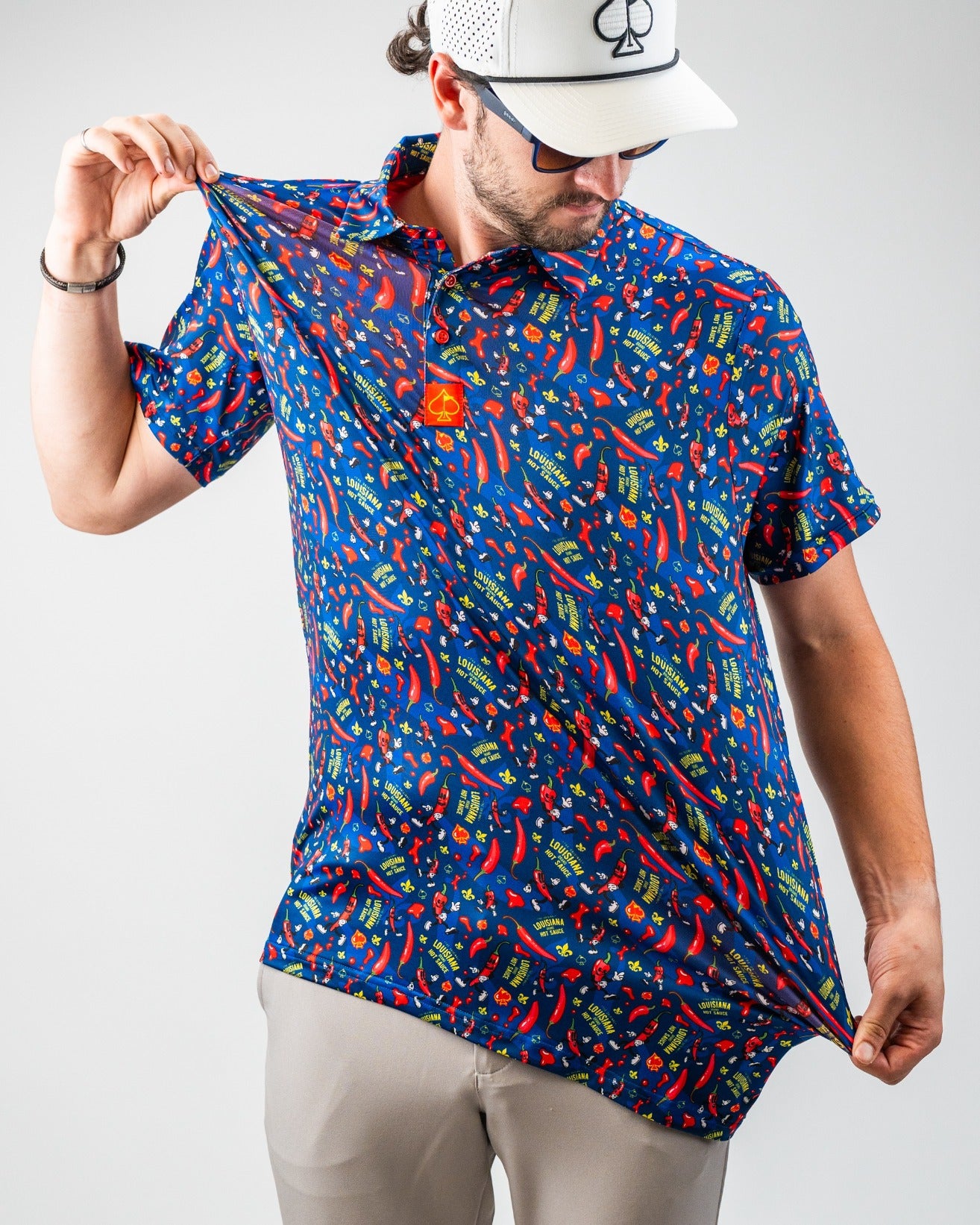 Man wearing a vibrant blue golf shirt with red chili pepper, "Louisiana" and "Hot Sauce" print, and a white cap with a spa...