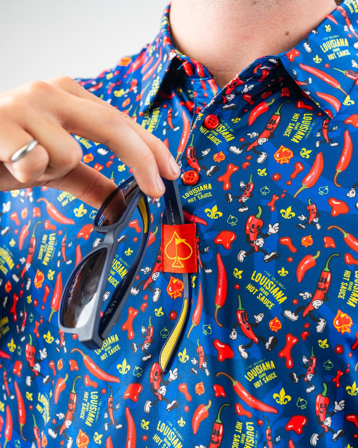 Bright blue shirt with red chili peppers, "Louisiana Hot Sauce" text, and playful mascot graphics, perfect for bold golf s...