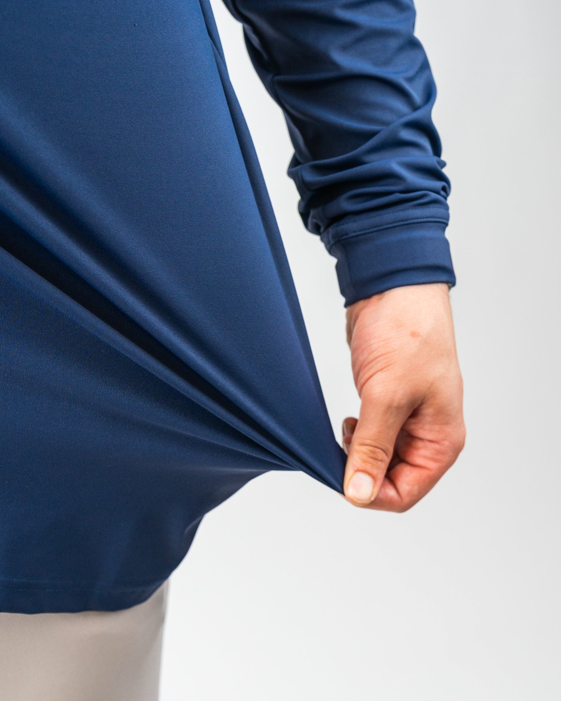 Close-up of a person pulling a navy blue, waterproof golf jacket, highlighting bold, vibrant color and sleek fabric design.