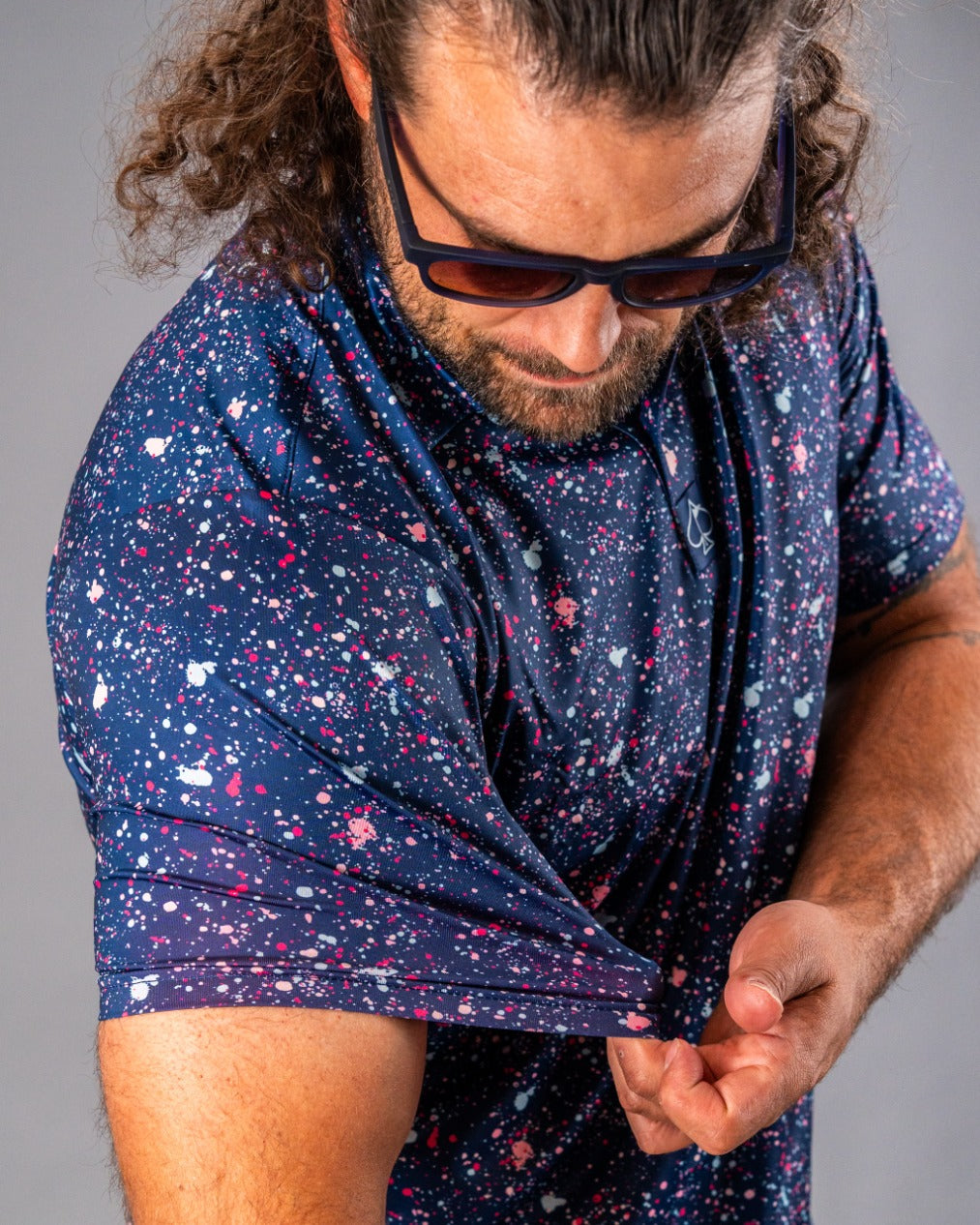 A golfer showcases a blue splatter polo shirt, highlighting its vibrant design and comfortable fit.