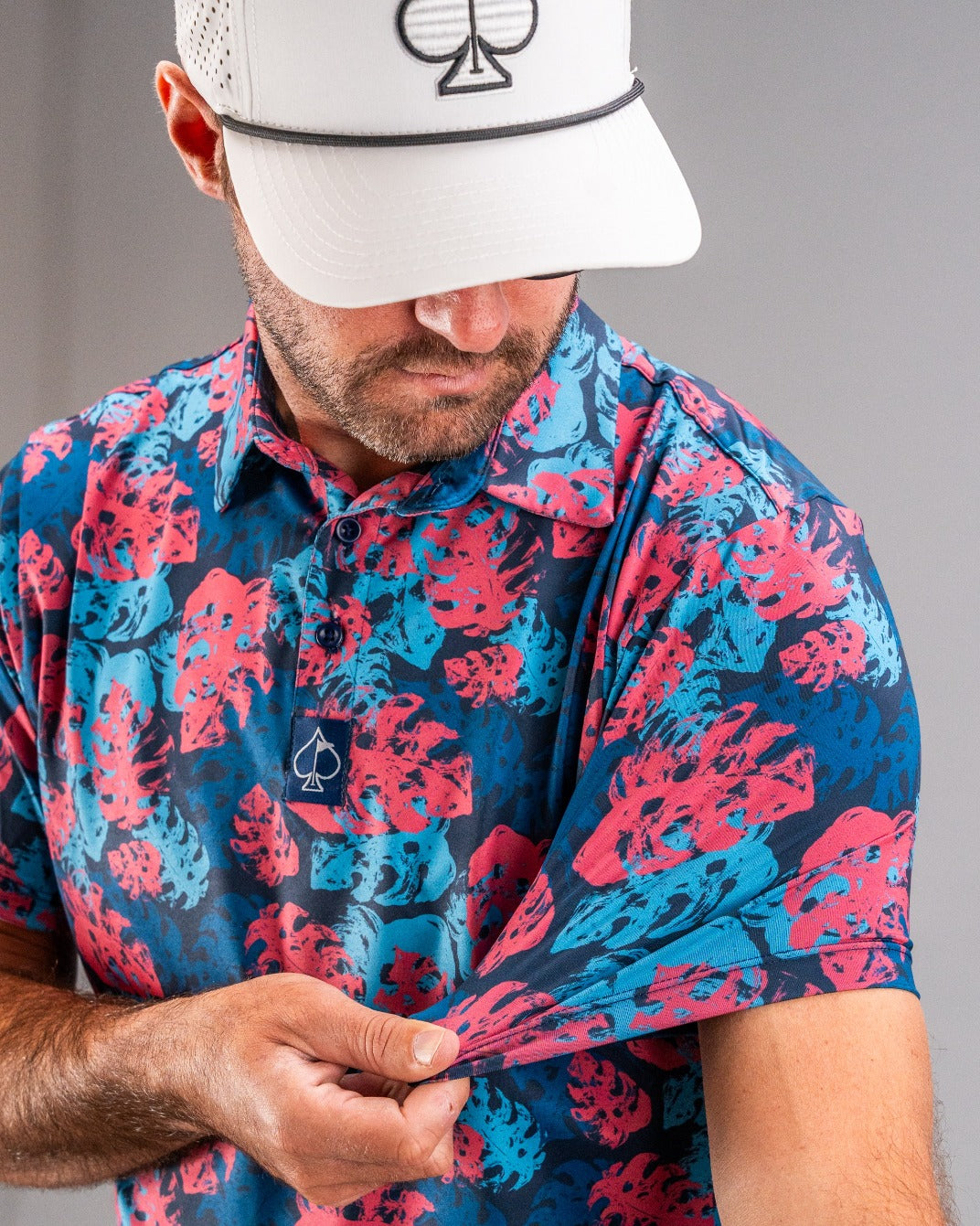 Bold golf polo featuring a vibrant blue and pink painted monstera leaf pattern, perfect for stylish golfers.