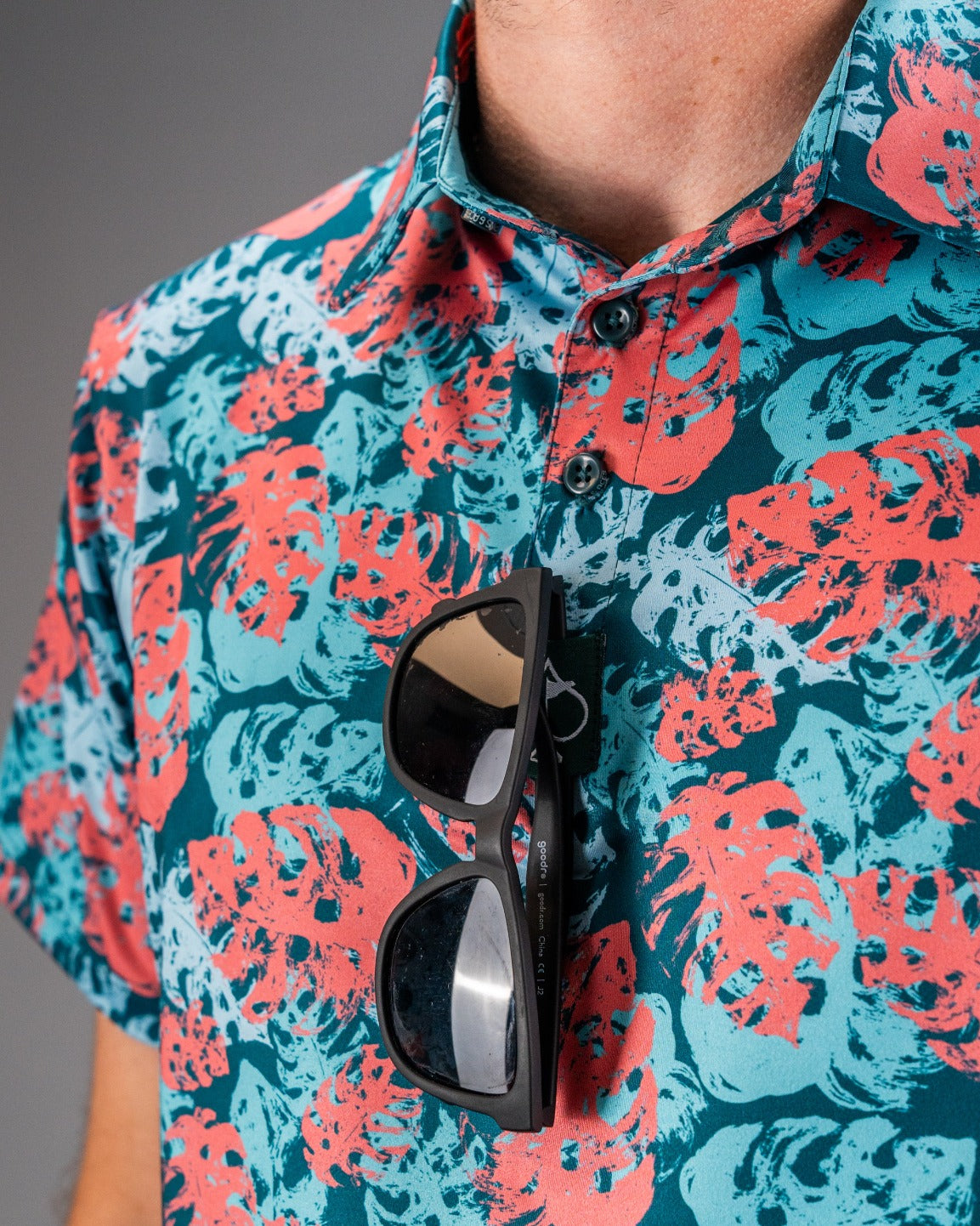 Bold painted monstera shirt in teal with vibrant red and white leaf patterns, featuring sunglasses resting on the collar.